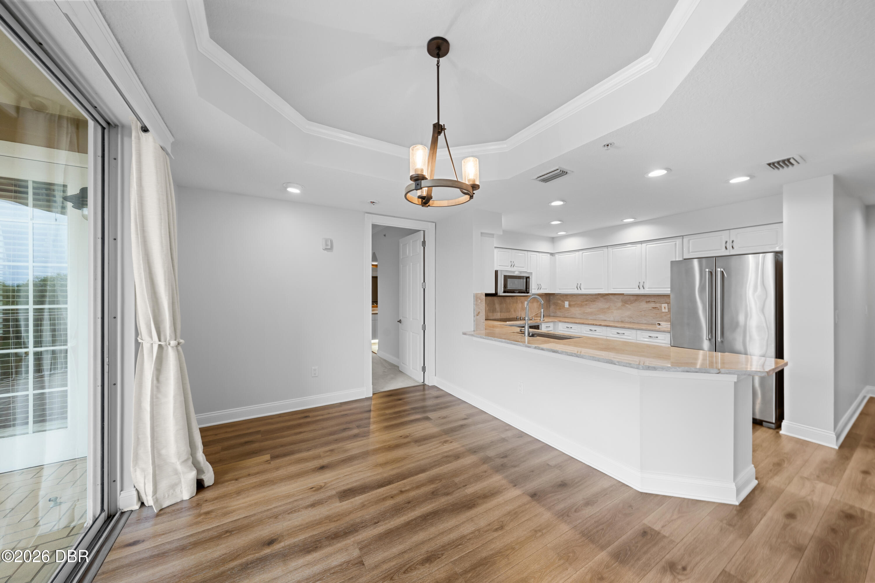 Vacant kitchen with white cabinets, stainless steel appliances, stone peninsula, and sliding glass doors.