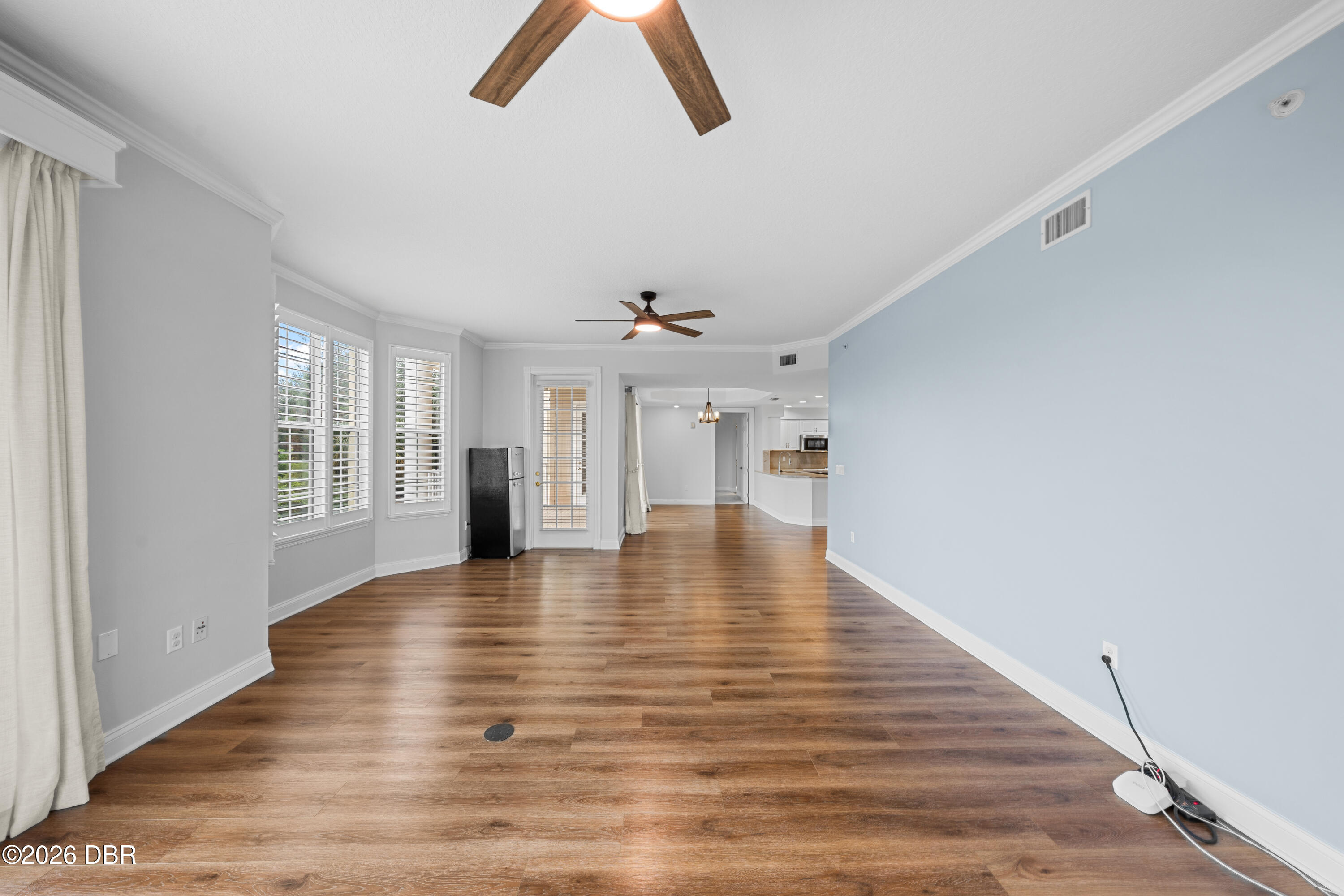 Unfurnished living area with wood-look floors, shuttered windows, and an open kitchen beyond.