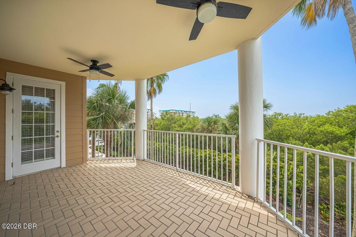 Covered tiled balcony with two ceiling fans and white railings overlooking palm trees and greenery.
