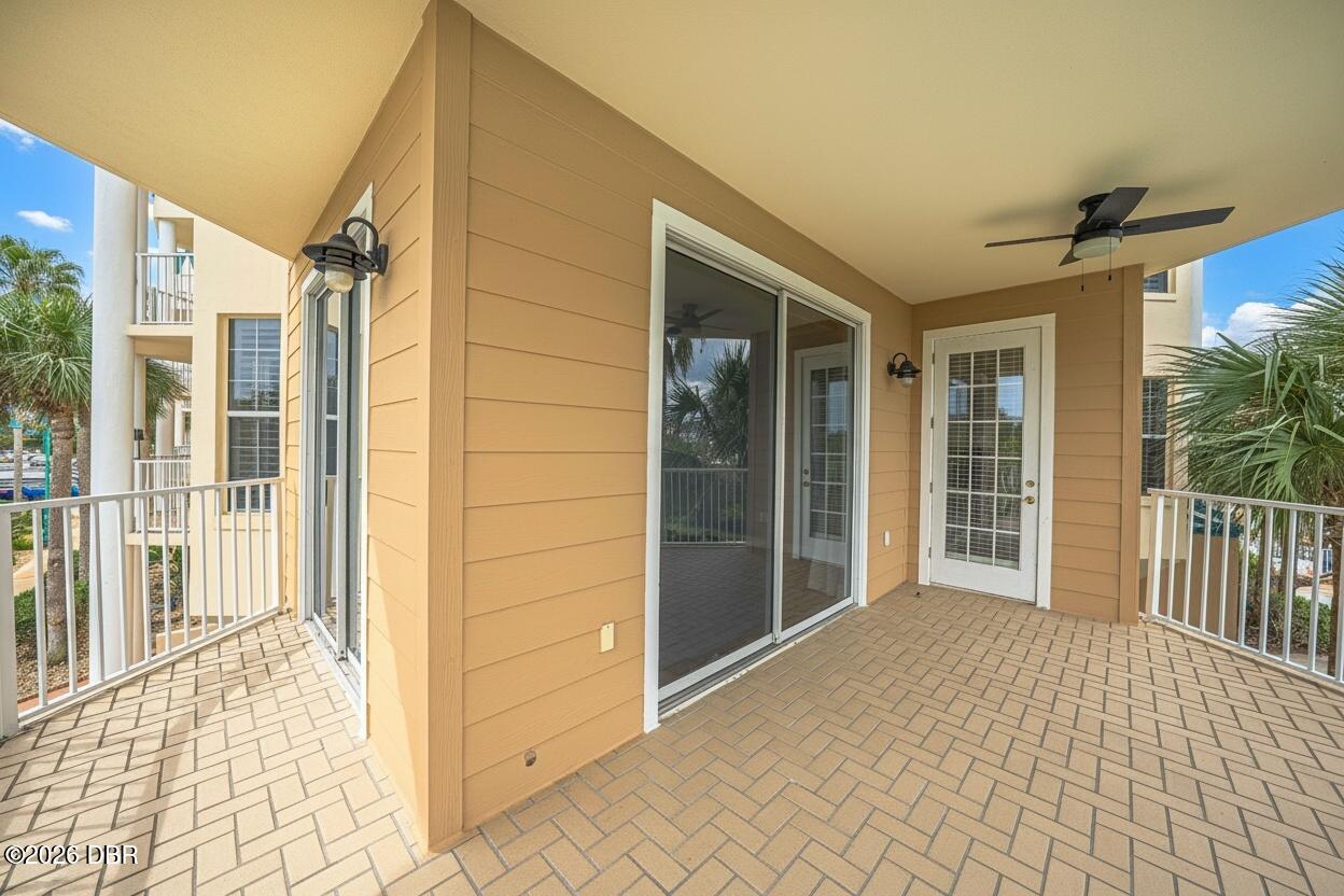 Covered balcony with tan siding, brick-pattern pavers, sliding glass door, and ceiling fan.