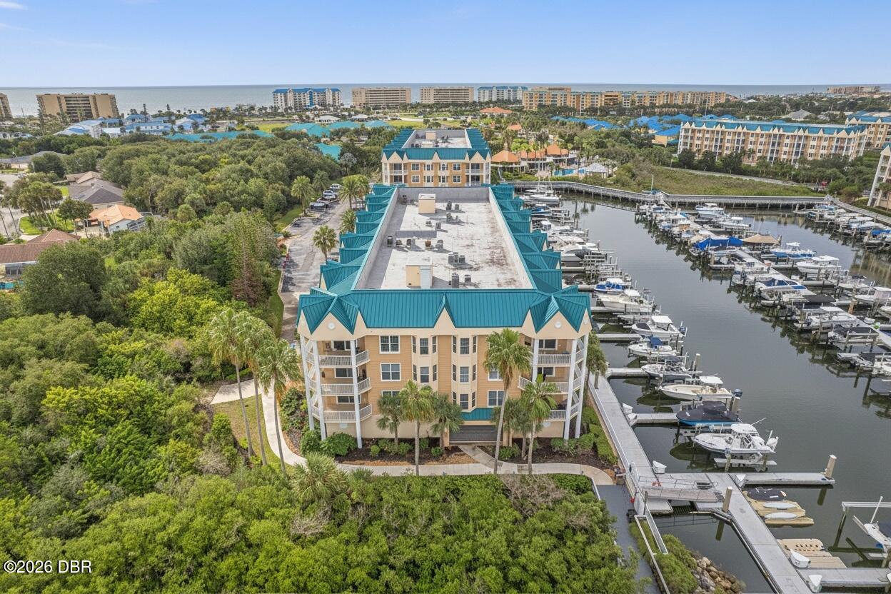 Condominium building with teal roofs beside a boat-filled marina, with the ocean on the horizon.