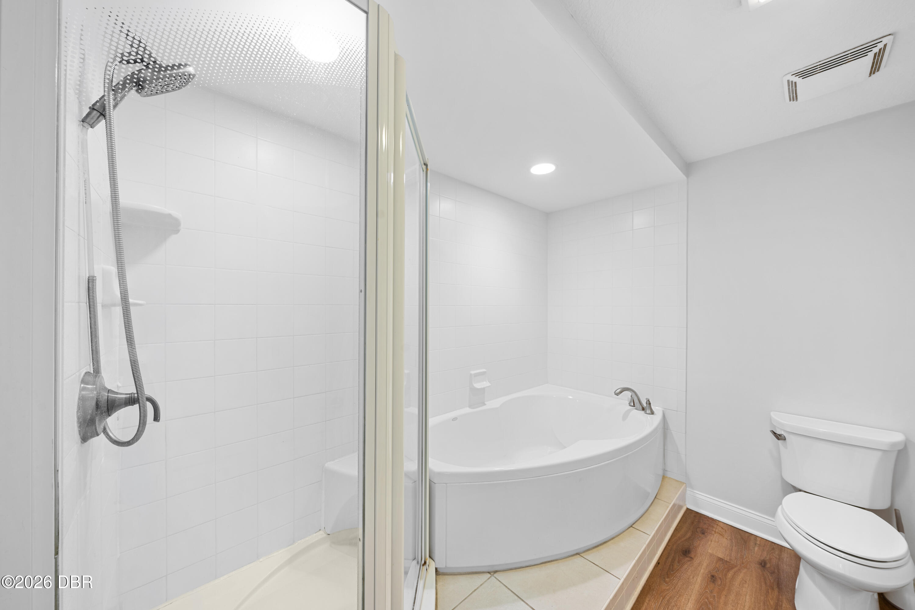 Bathroom with glass-enclosed shower, raised corner soaking tub, and toilet.