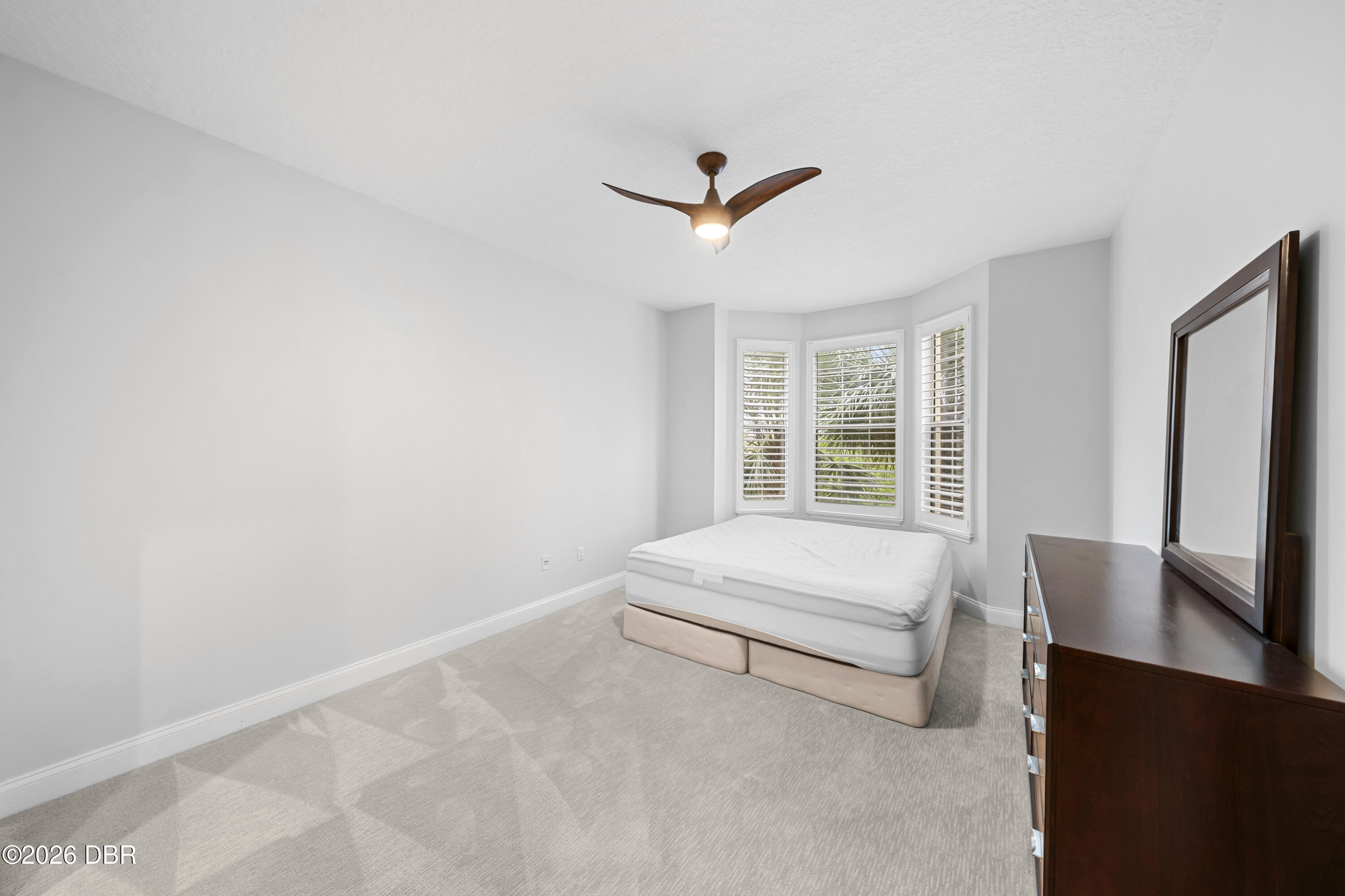 Bedroom with a low bed beneath three shuttered windows and a wood ceiling fan.