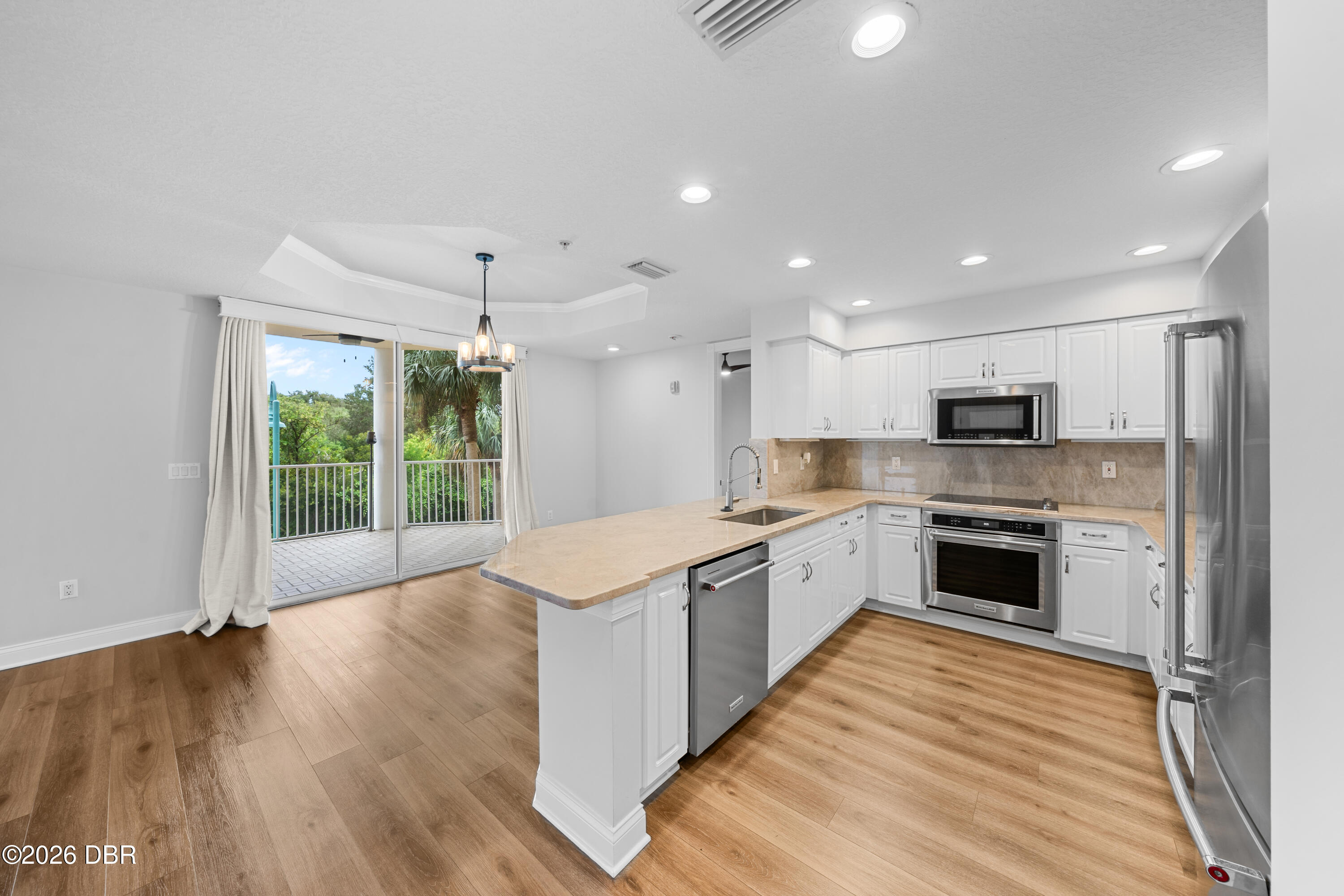 Bright kitchen with a large peninsula island and sliding doors to a tree-lined balcony.
