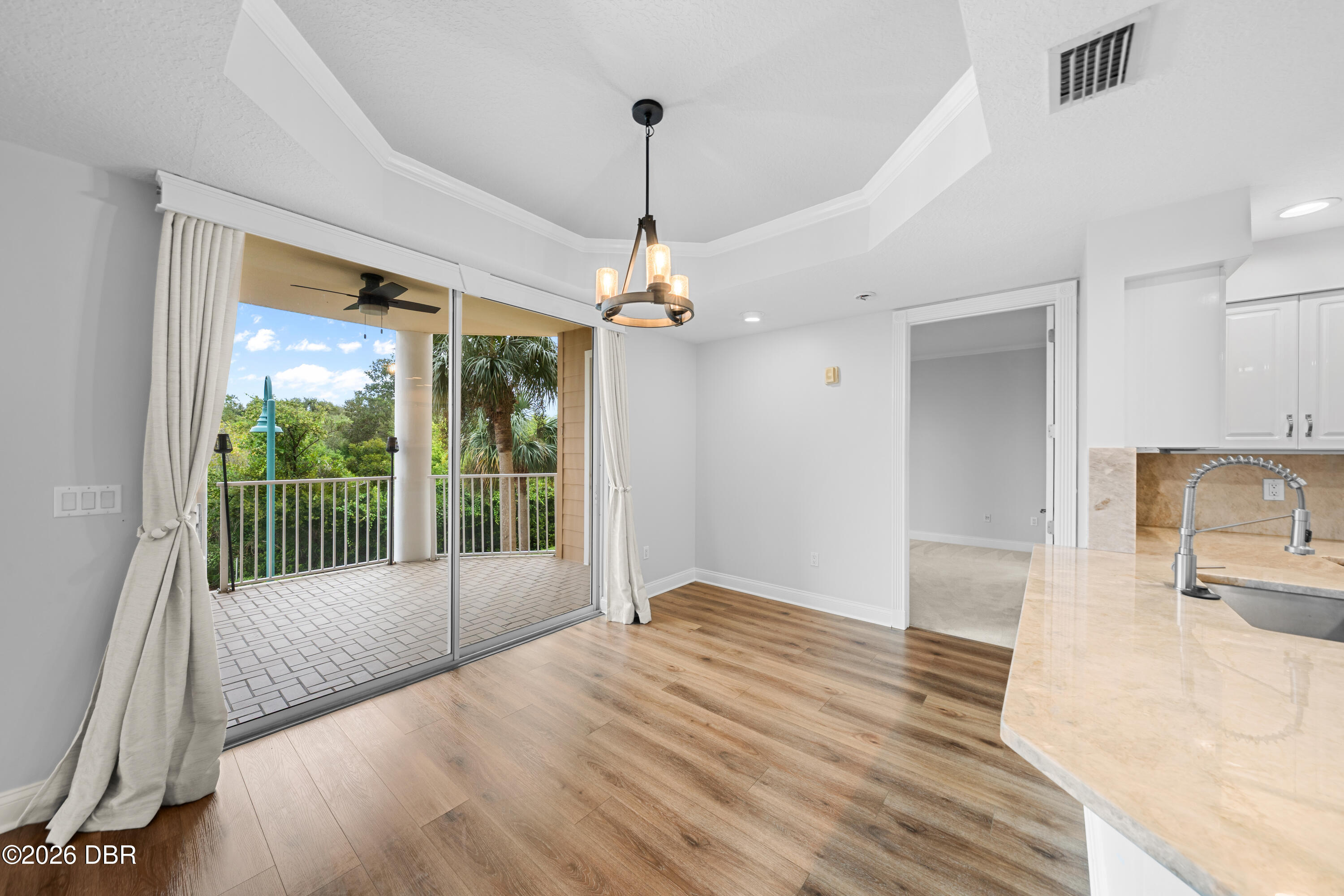 Dining area with wood floors and sliding doors opening to a tiled balcony surrounded by greenery.