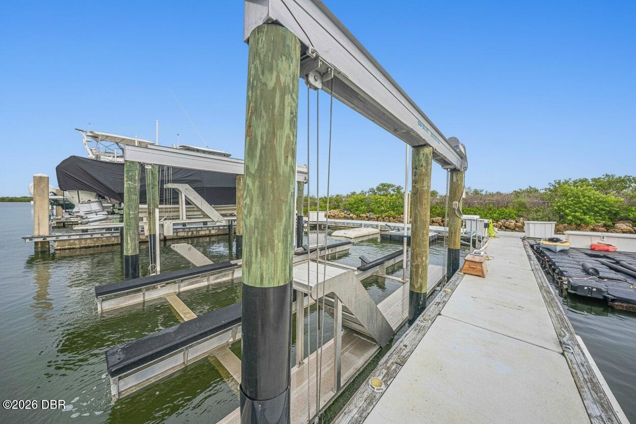 Boat dock with a boat lift, covered boat, and concrete walkway along the water.