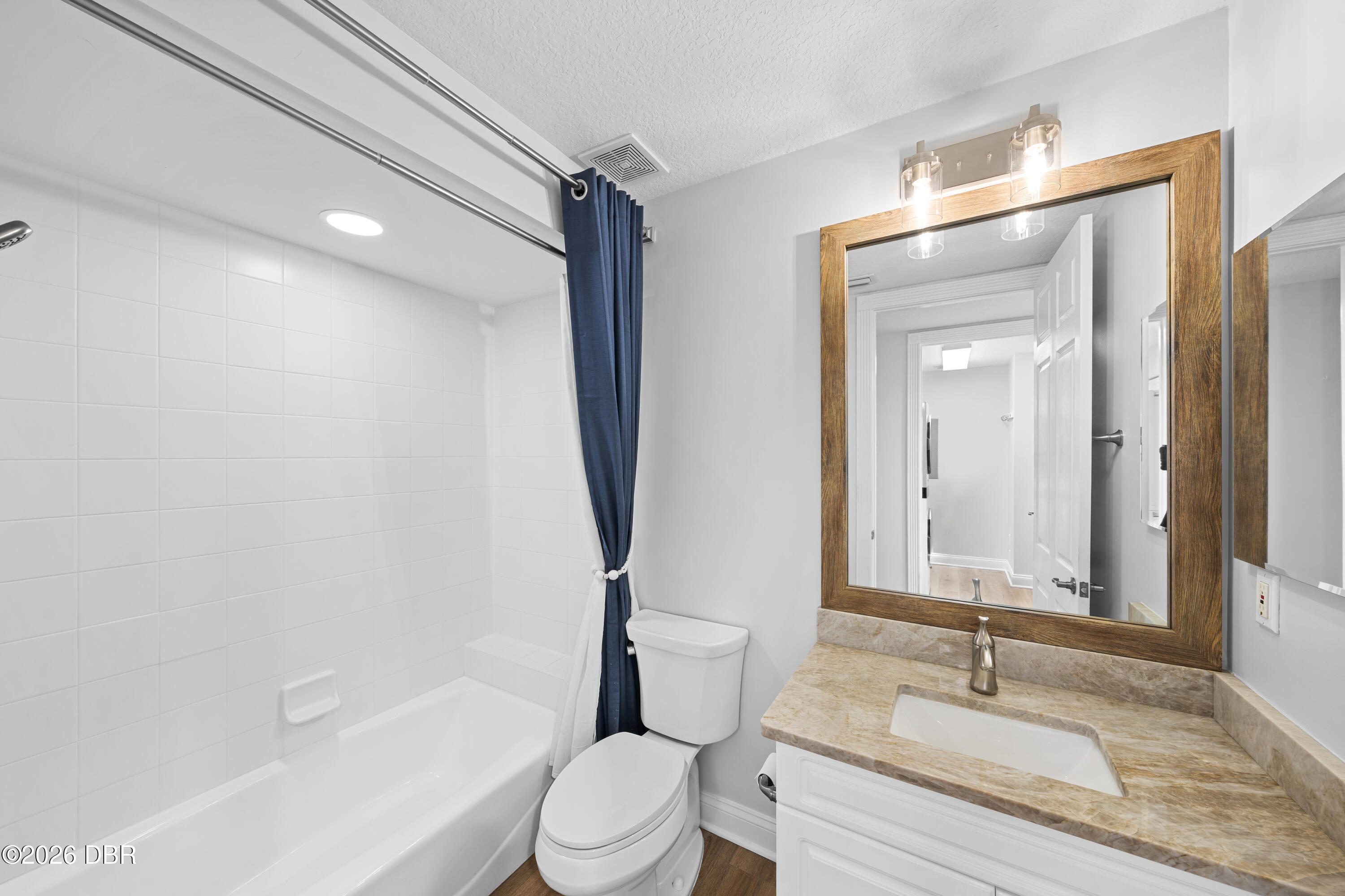 Bathroom with tiled tub, navy shower curtain, toilet, and marble-look vanity.