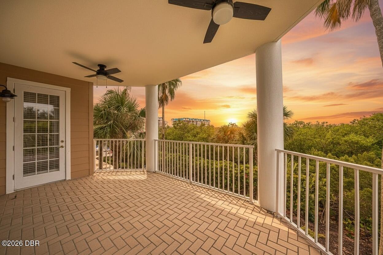 Covered patio with brick-pattern pavers and white railings overlooks palms at sunset.