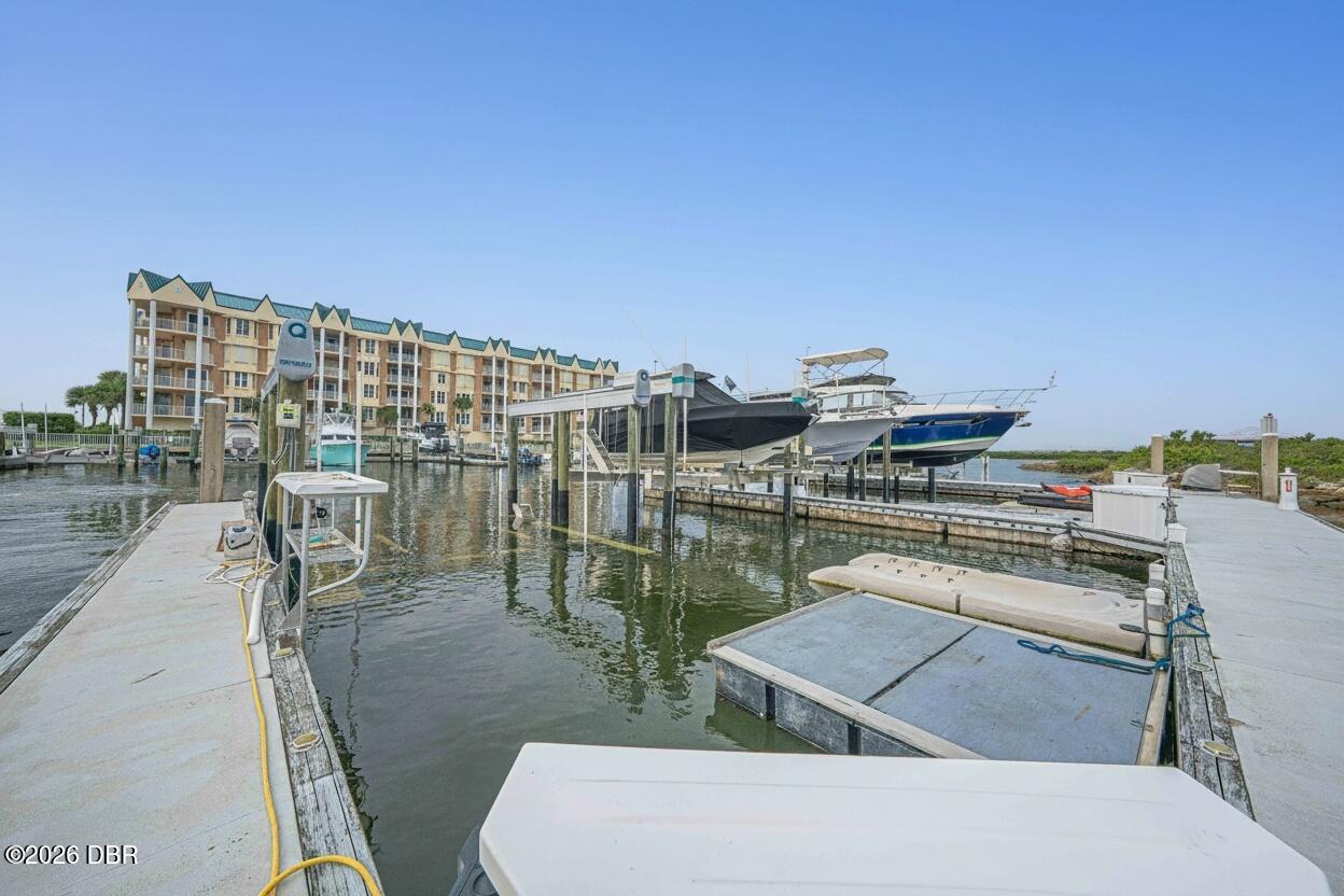 Marina boat slips and docked boats with a waterfront condominium building behind them.