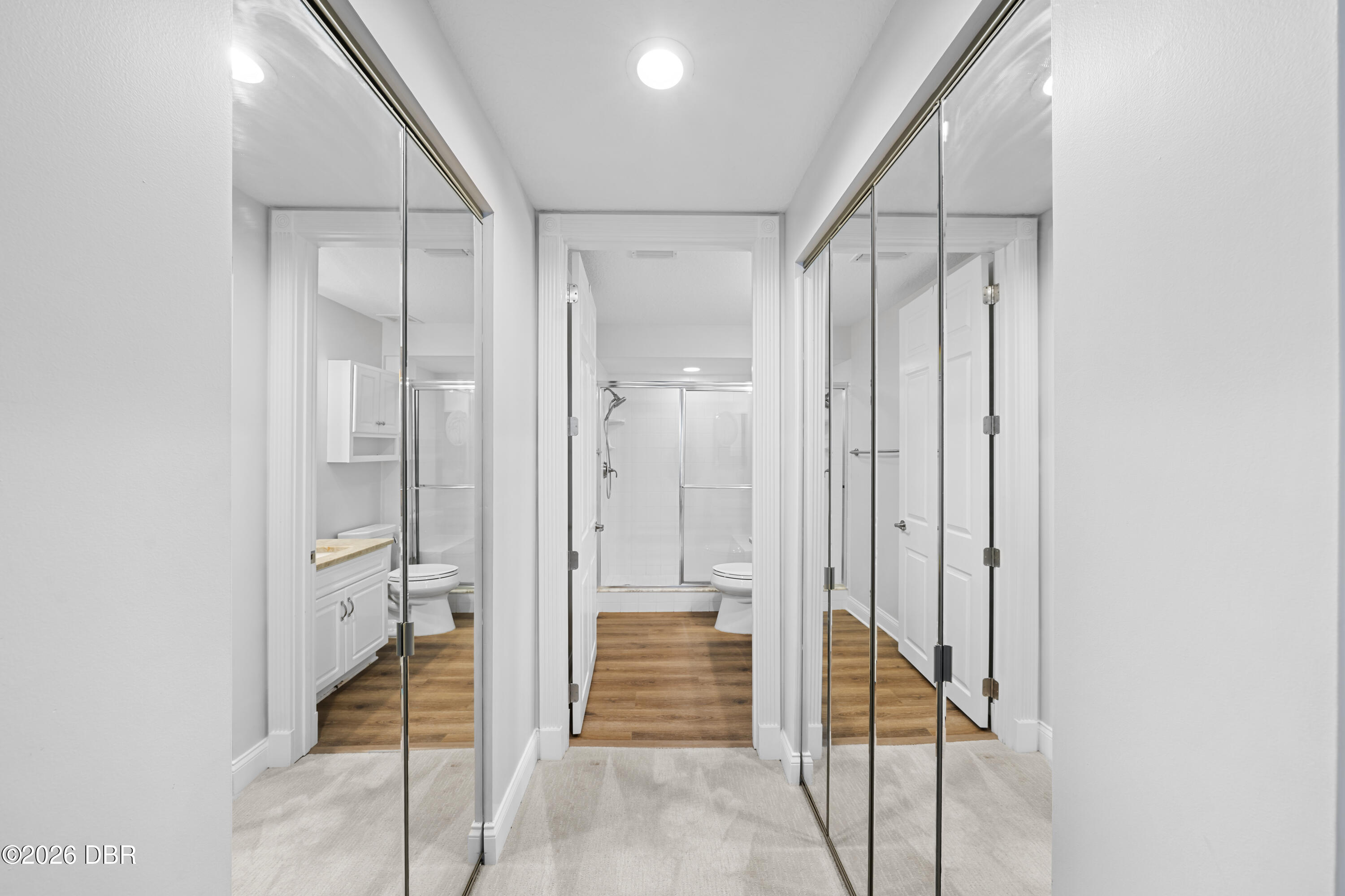 Bathroom with mirrored closet doors, a white vanity, toilet, and glass-enclosed shower.