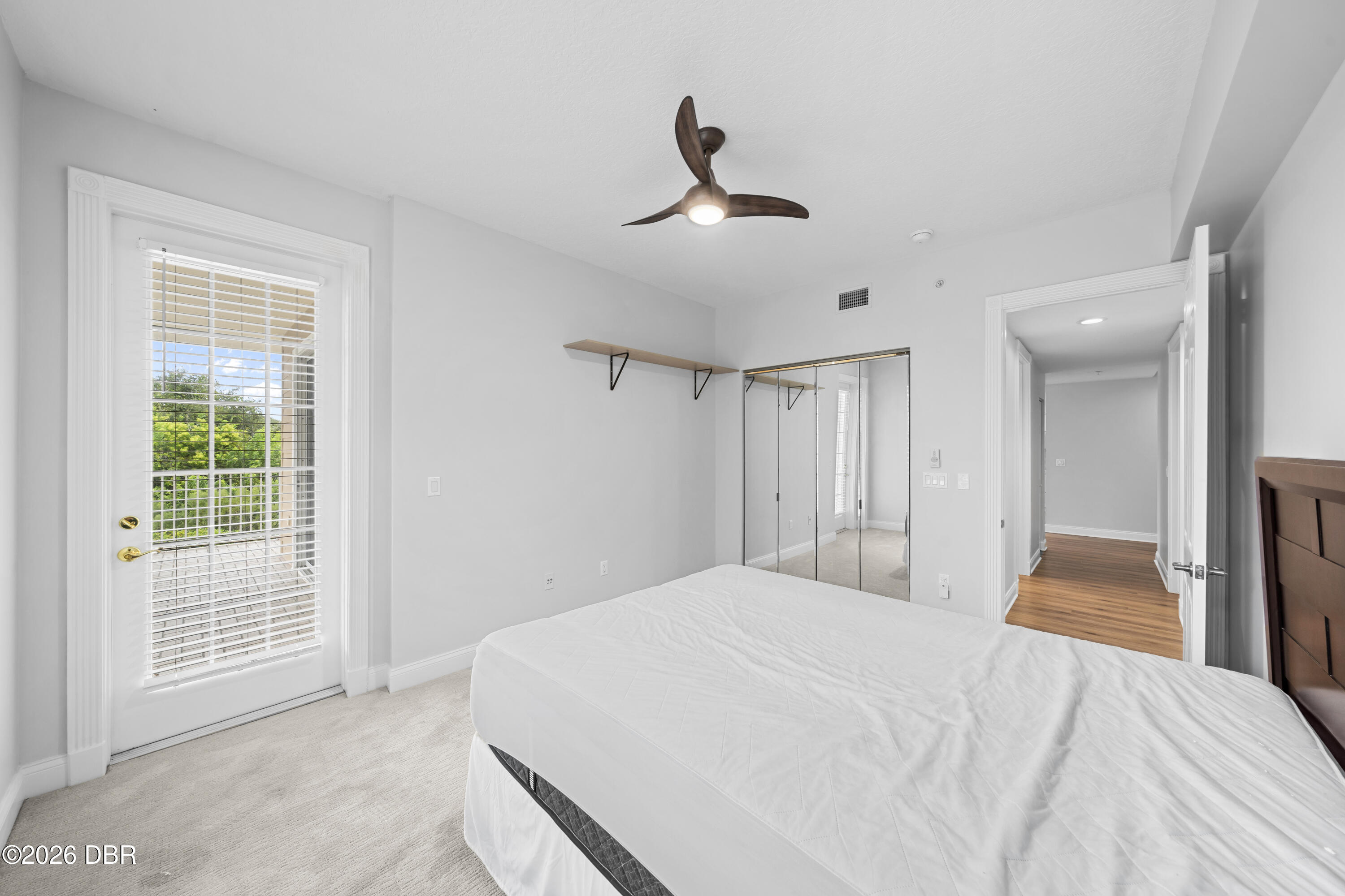 Bedroom with mirrored closet doors and a glass balcony door with blinds.