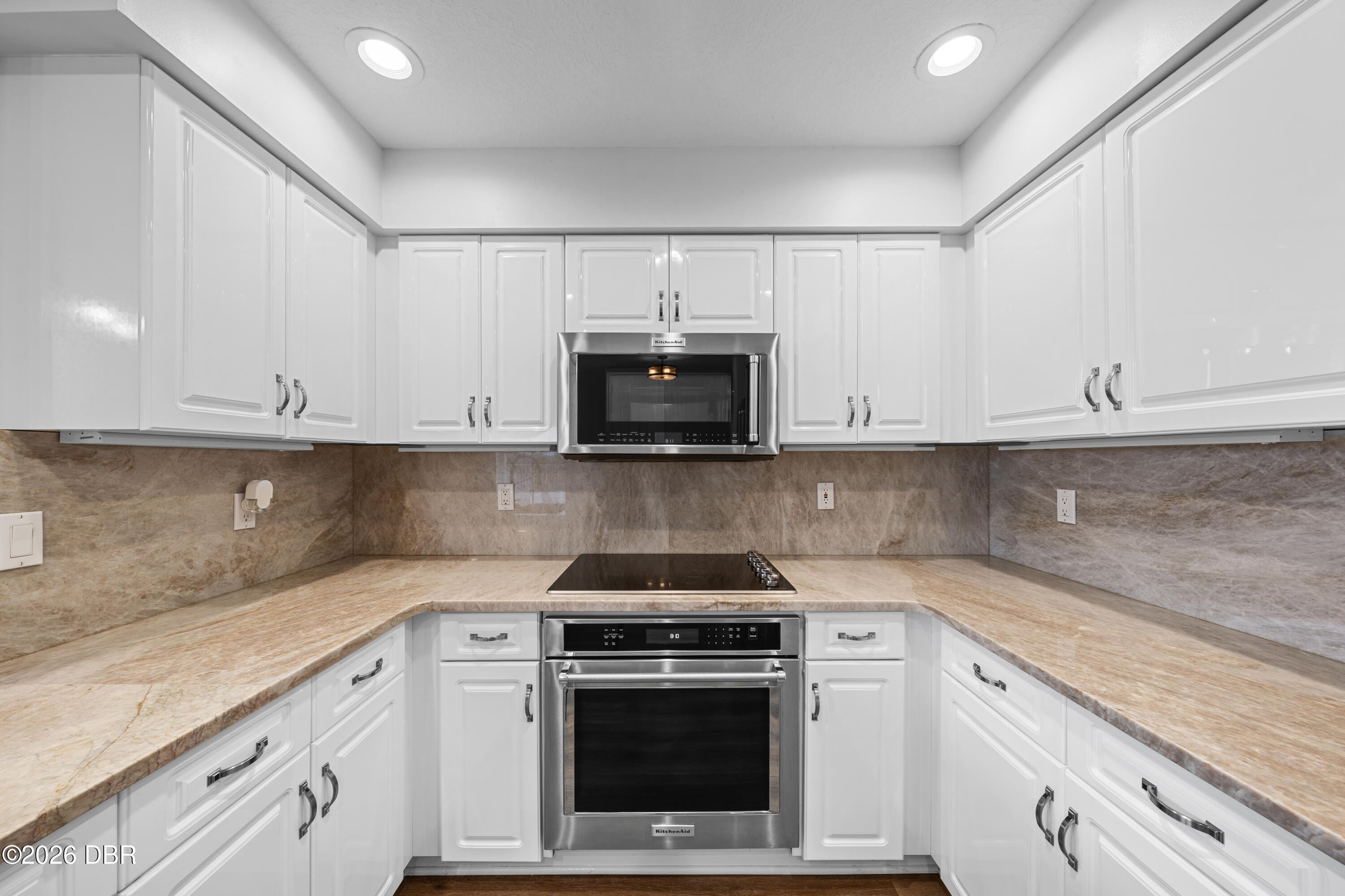 Kitchen with white cabinets, beige stone counters, and stainless steel oven and microwave.