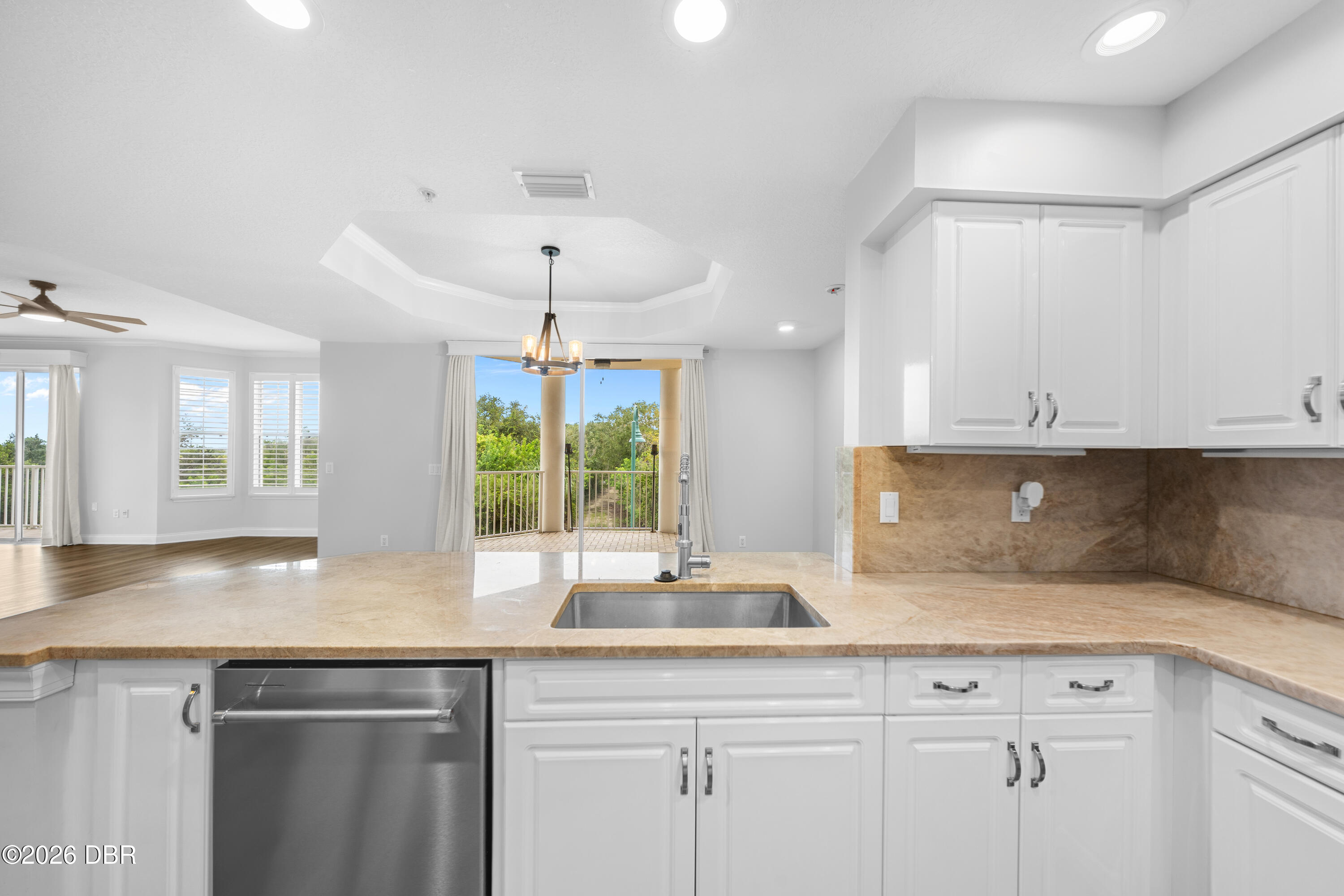 Bright kitchen with white cabinets, tan stone counters, stainless dishwasher, and balcony access.