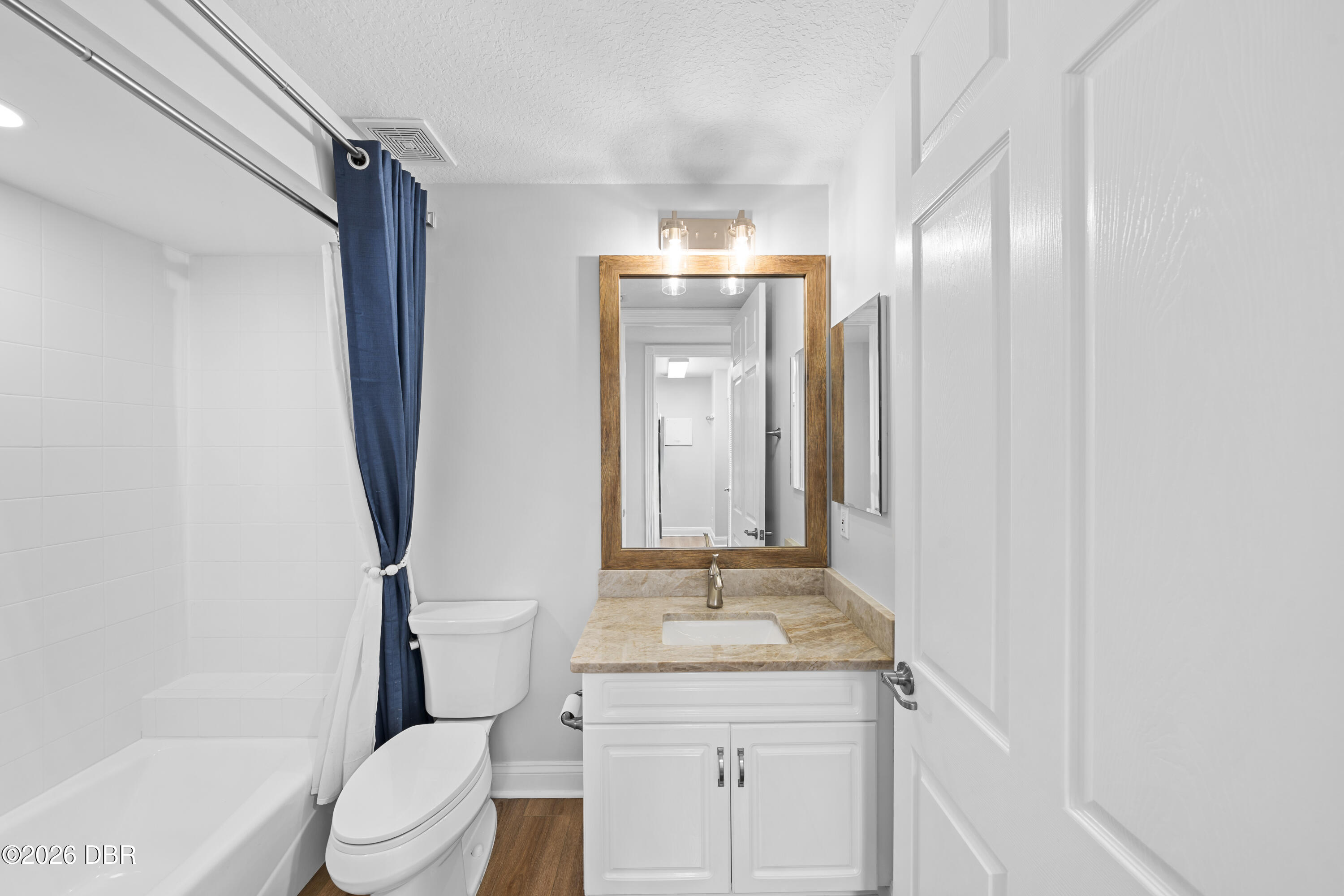 Bathroom with a navy shower curtain and white vanity topped with tan stone.