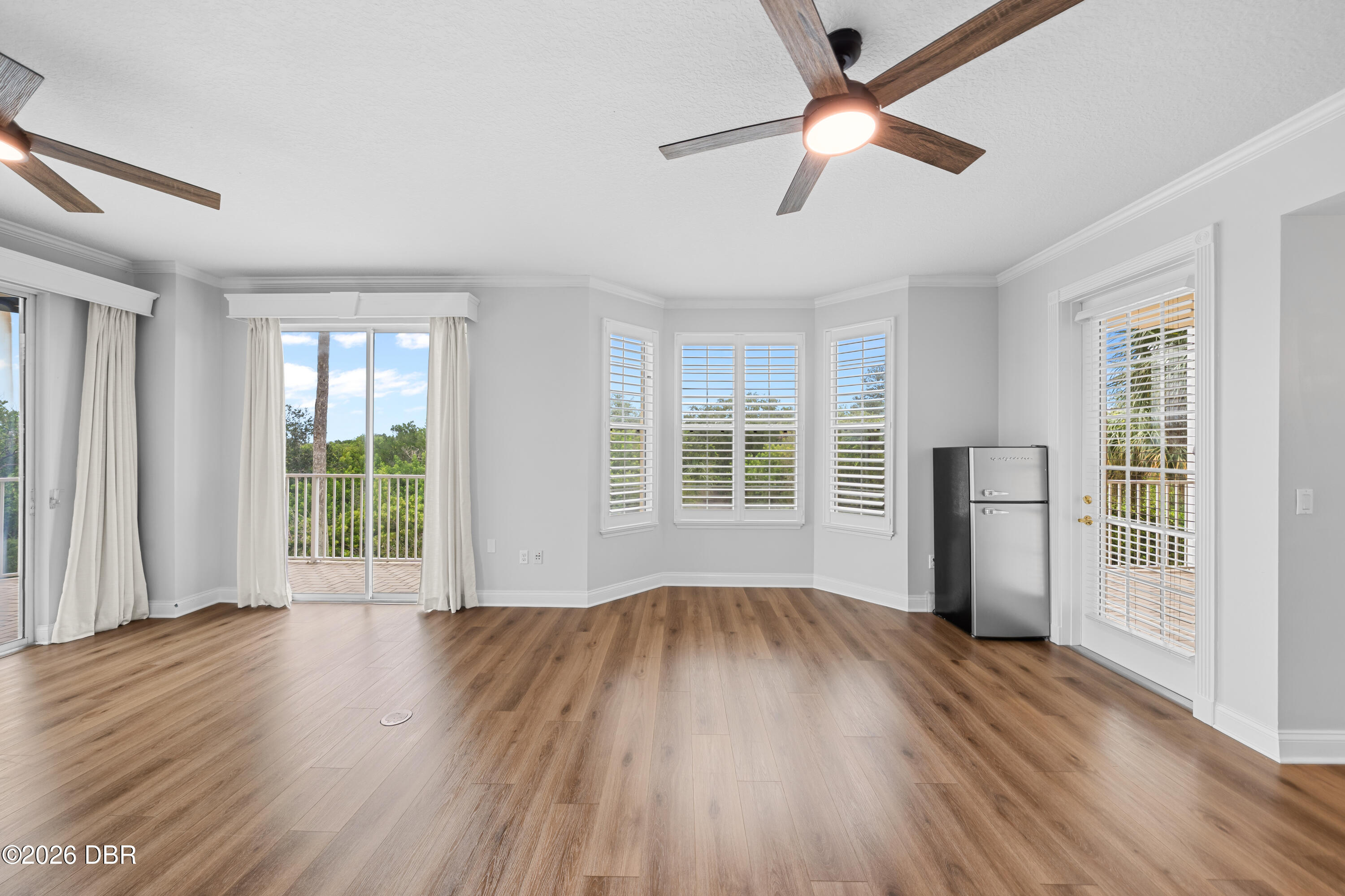 Vacant room with wood-look floors, plantation shutters, and glass doors opening onto a balcony.