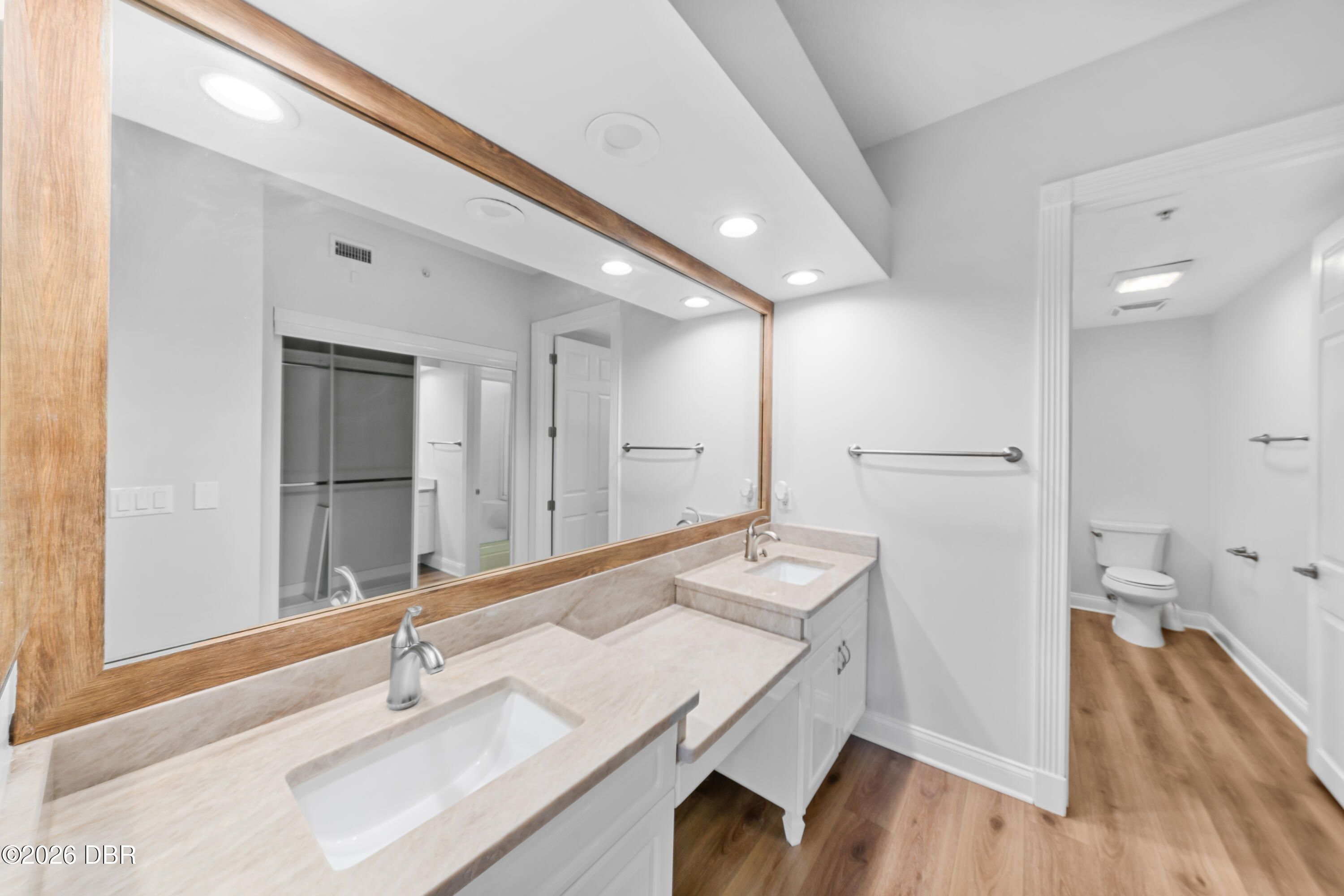 Bathroom with double vanity, pale stone counters, large wood-framed mirror, and separate toilet area.