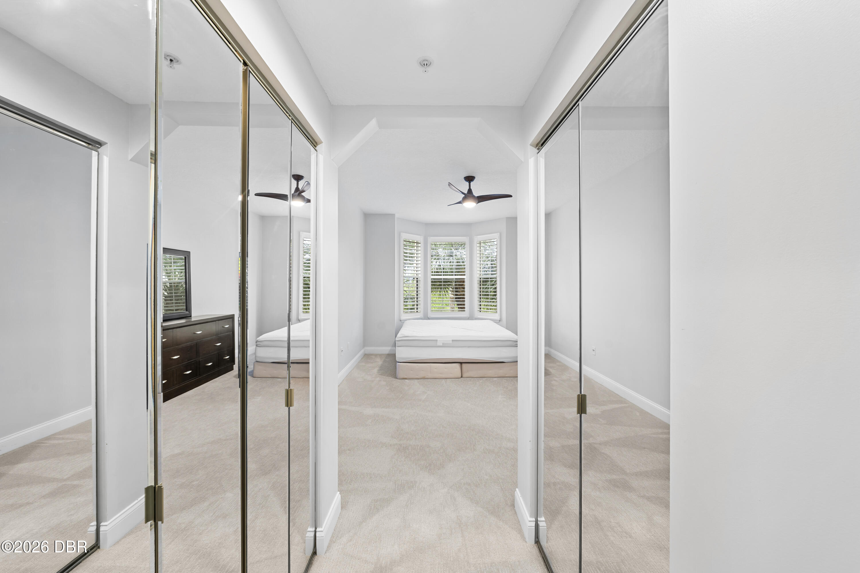 Bedroom with mirrored closet doors, a bed, and shuttered bay windows.
