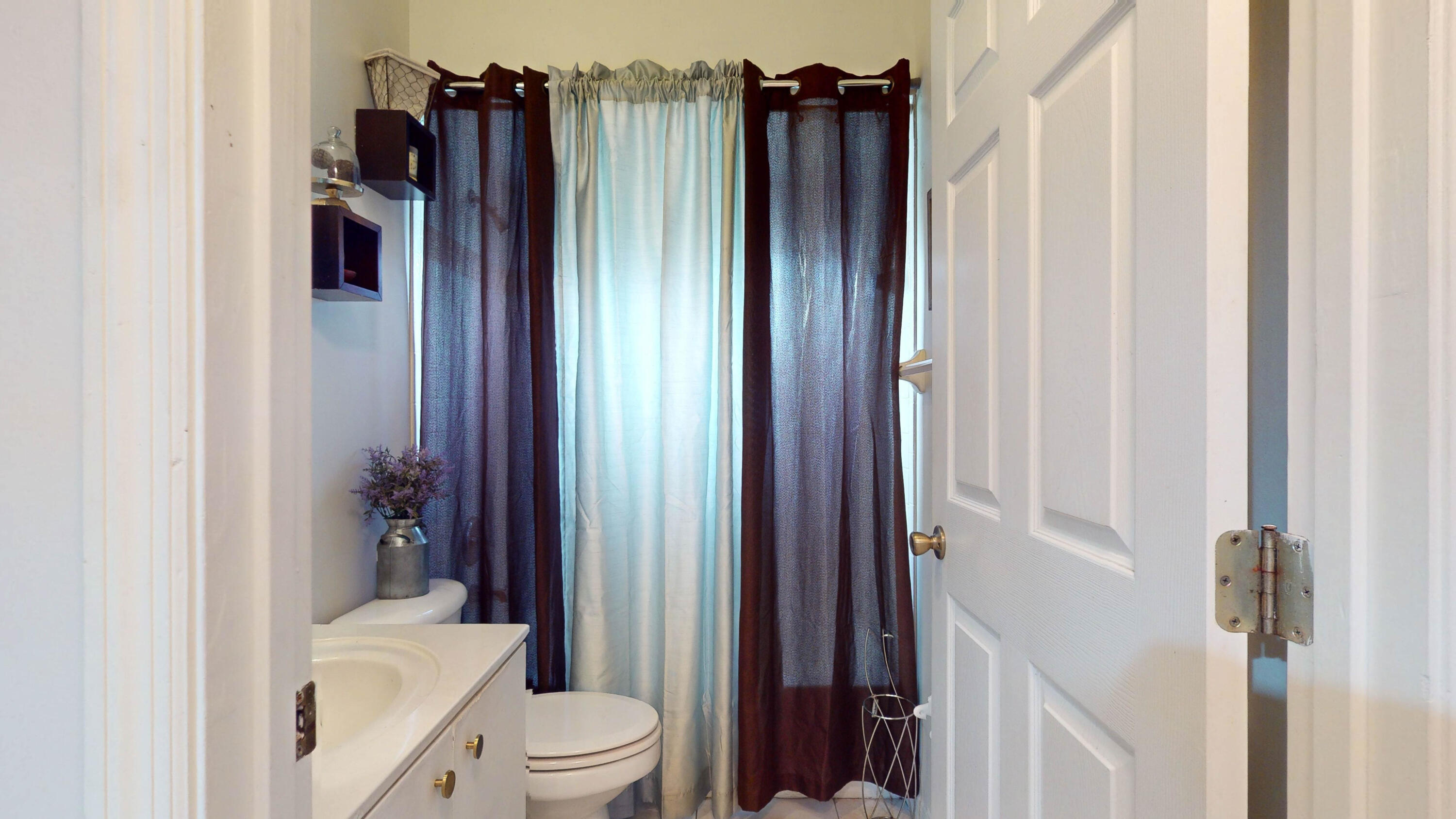 Bathroom with white vanity and toilet, framed by dark blue and burgundy curtains.