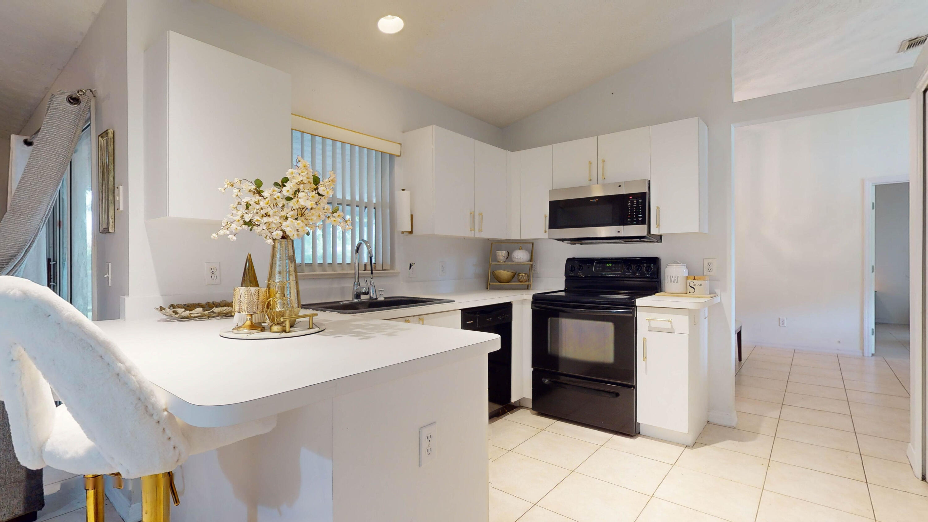 Bright white kitchen with black appliances, a breakfast bar, and upholstered stools.