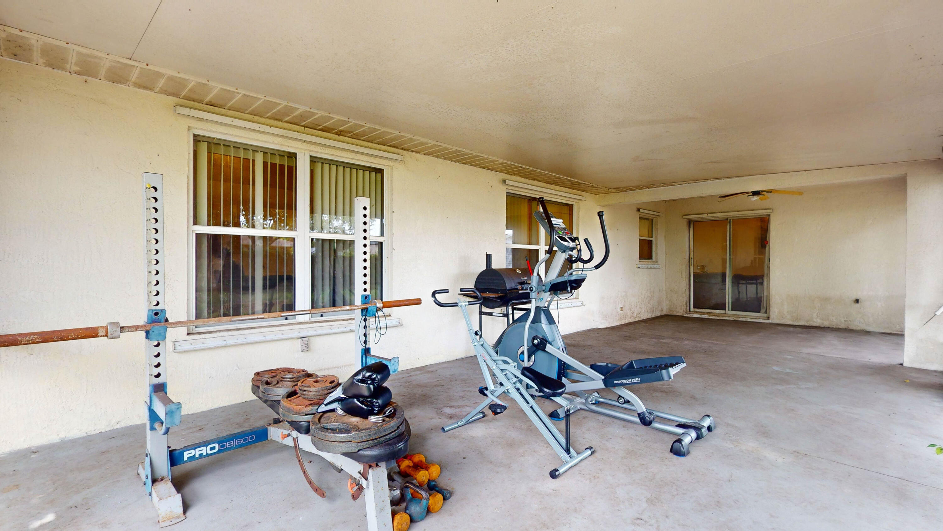 Covered exercise area with a weight bench, free weights, and an elliptical machine.
