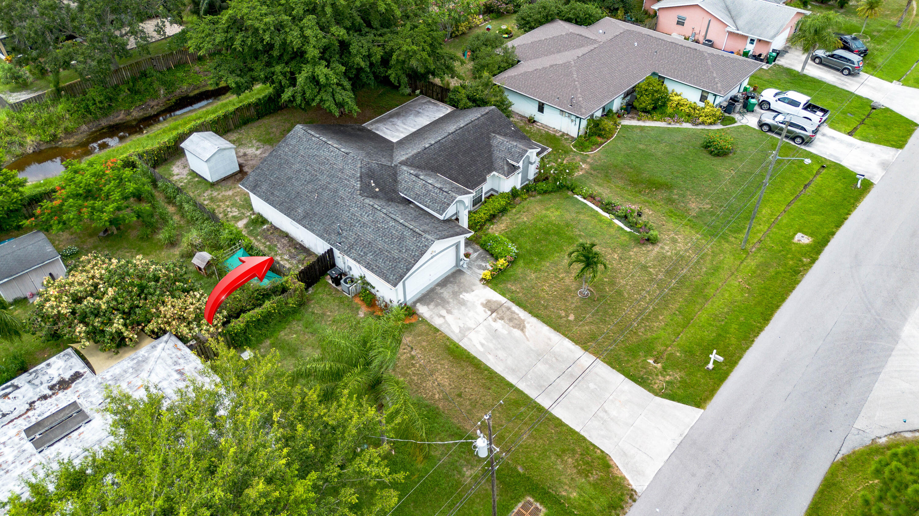 Aerial view of a white home with a gray roof, fenced yard, and canal behind it.