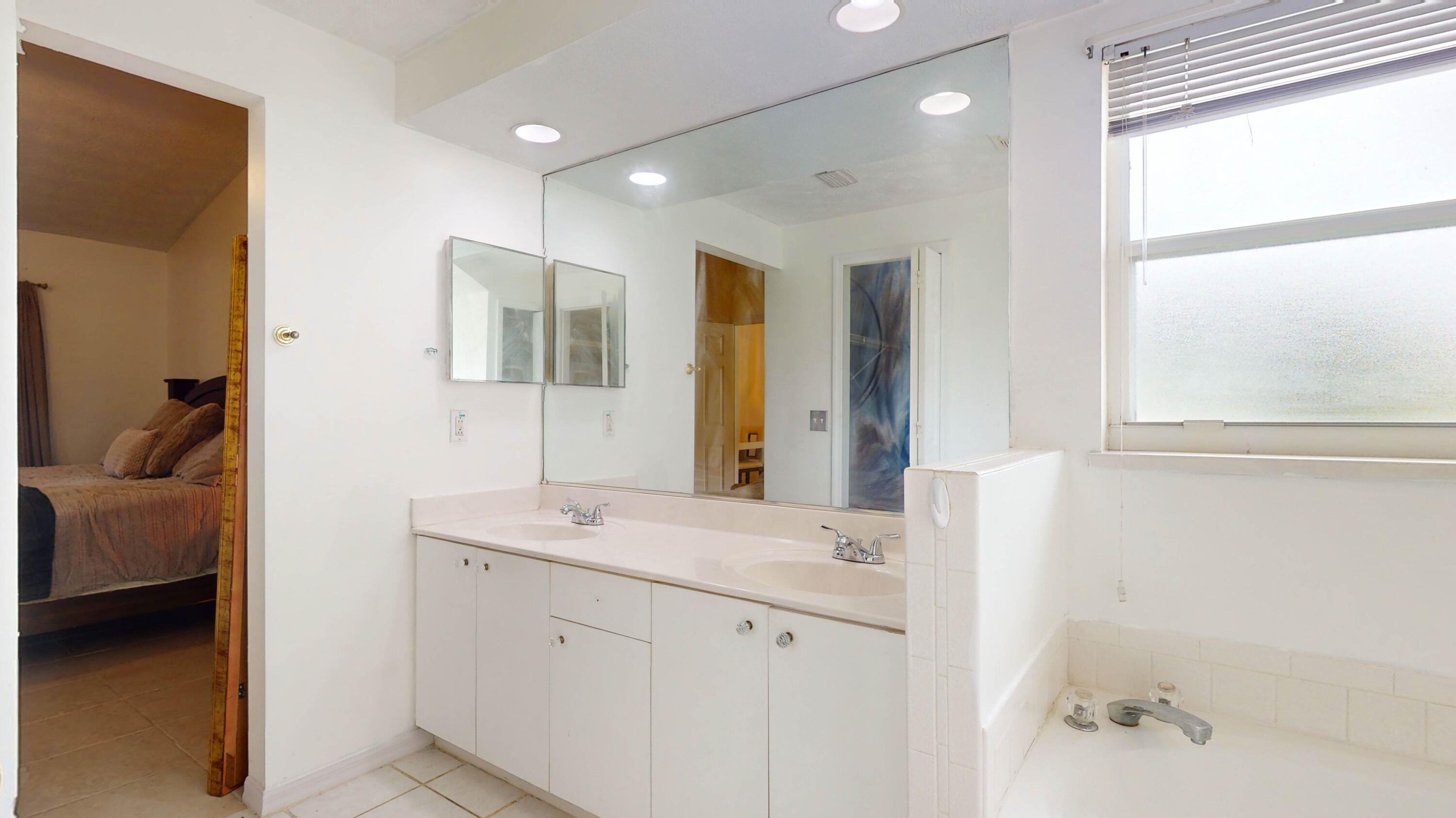 Bathroom with a double-sink vanity, large mirror, and bathtub beside a bright window.