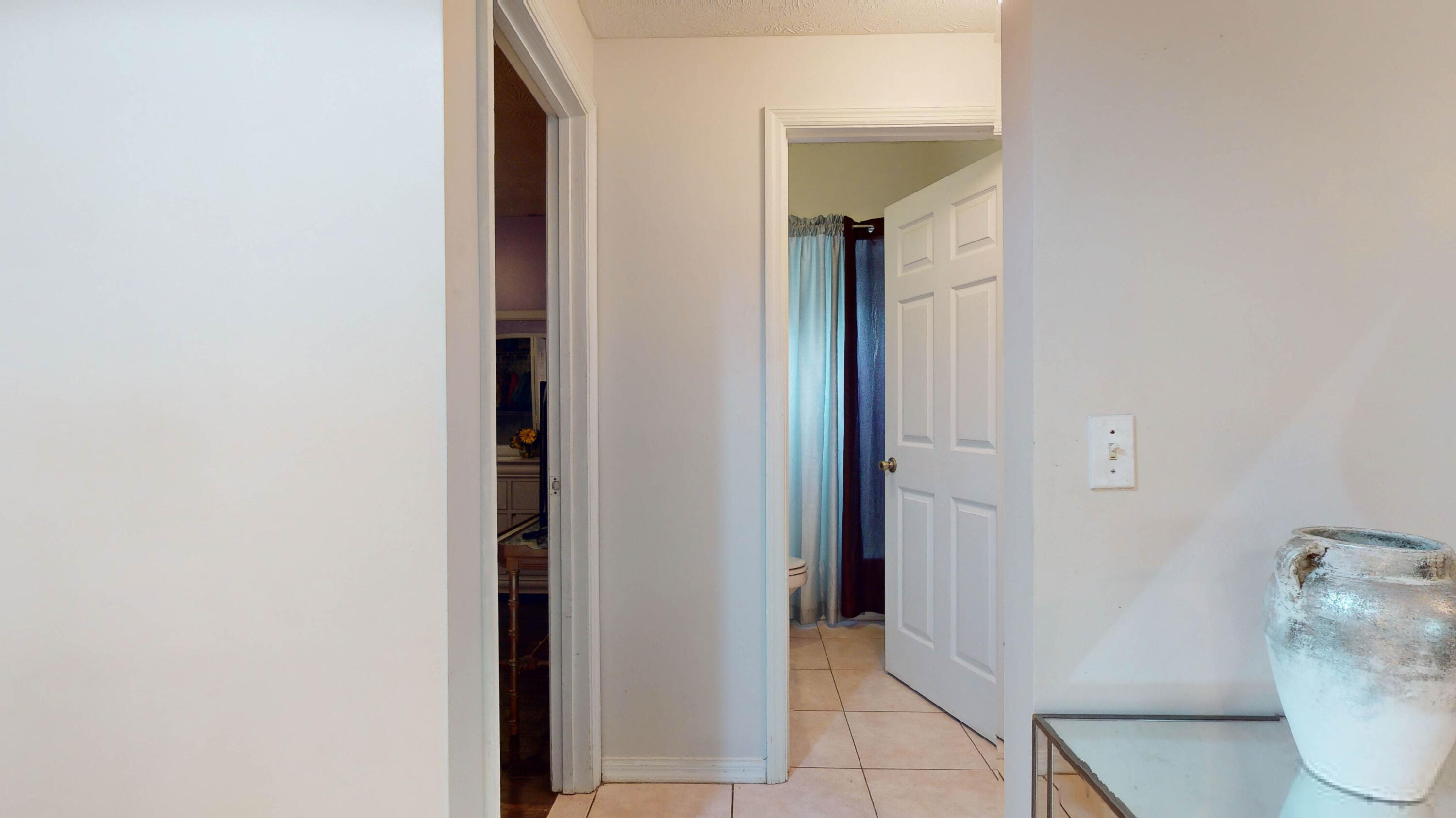 Tiled hallway with open doorways and a glass console table topped by a large vase.