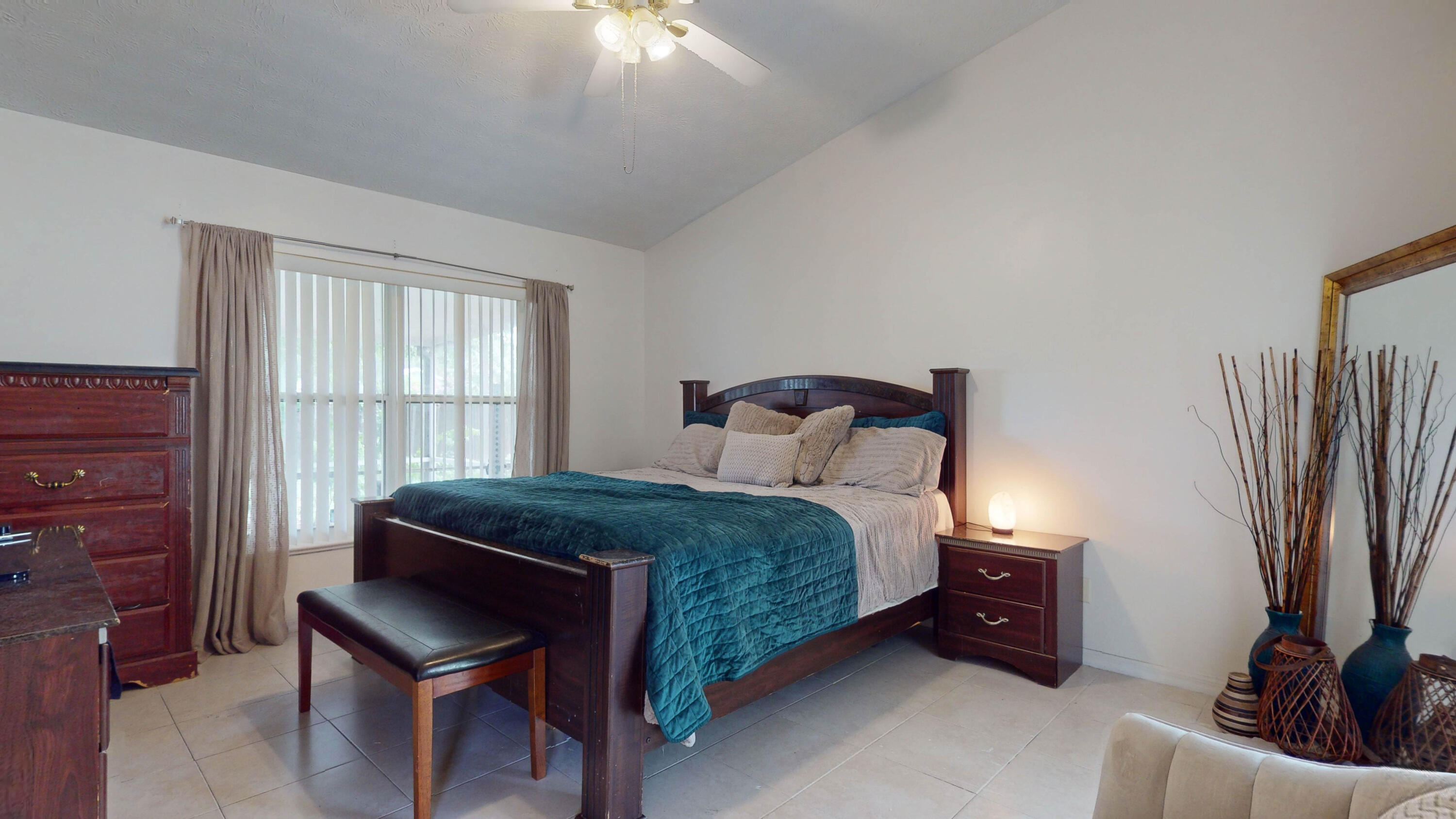 Furnished bedroom with a dark wood bed, teal quilt, and sliding window with vertical blinds.