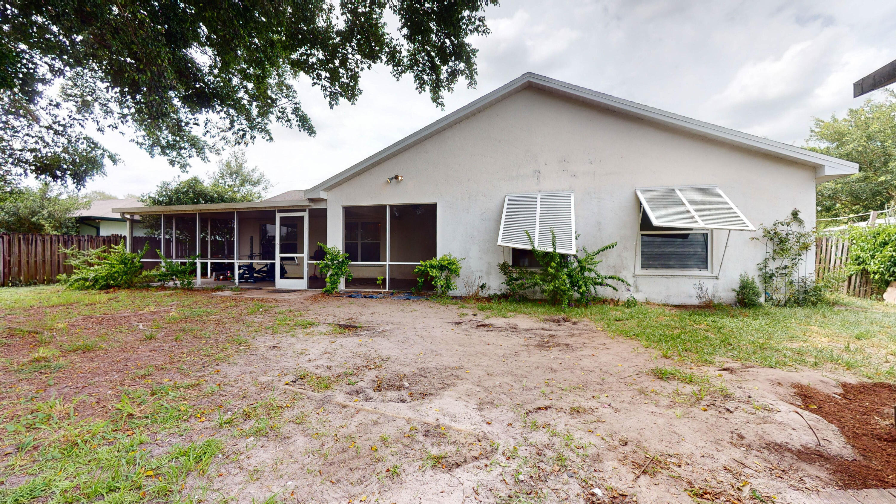 Rear of a white single-story house with a screened porch and sparse sandy yard.