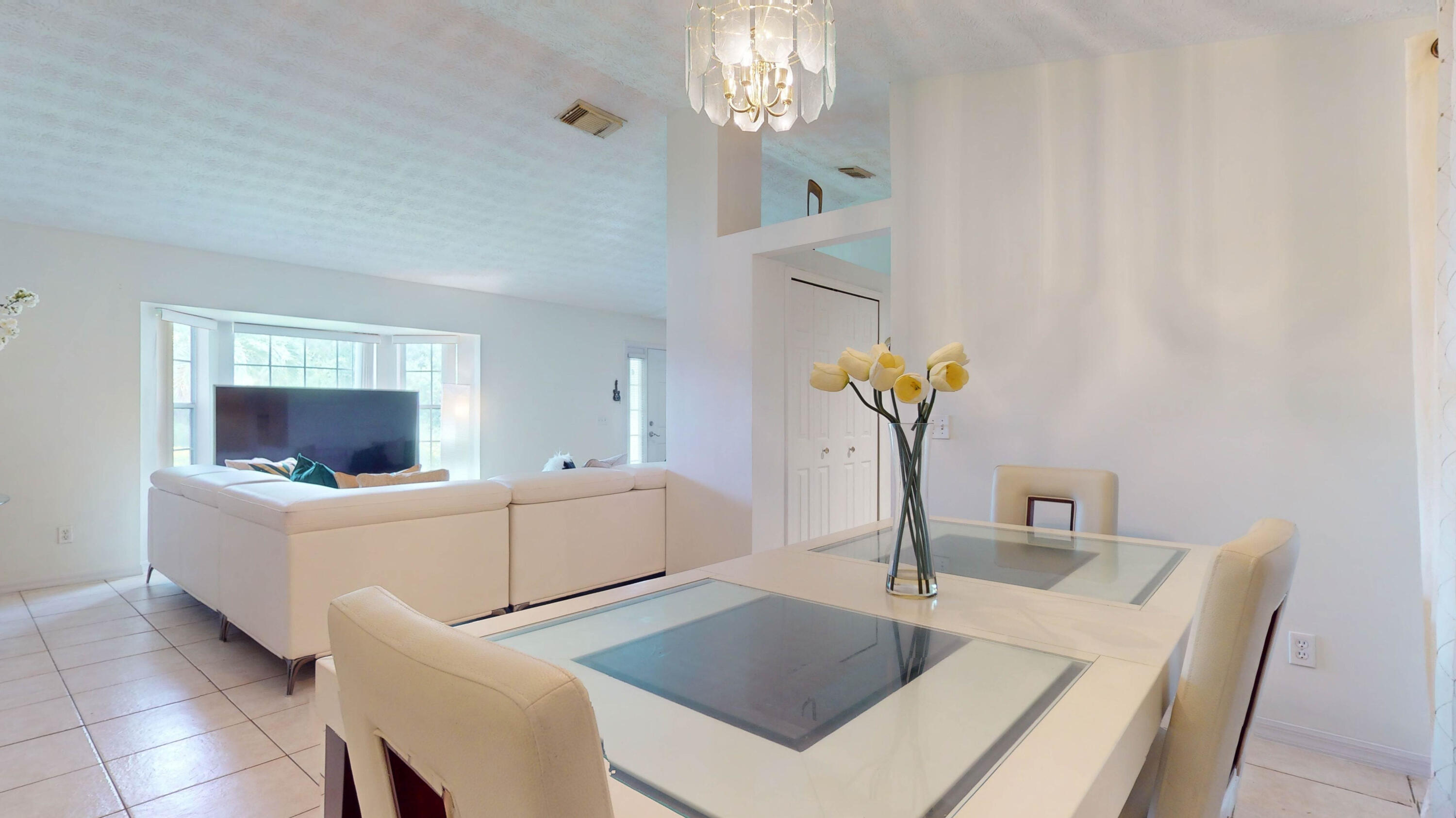 Dining area with a glass-top table and chandelier opening onto a living room with a white sectional.