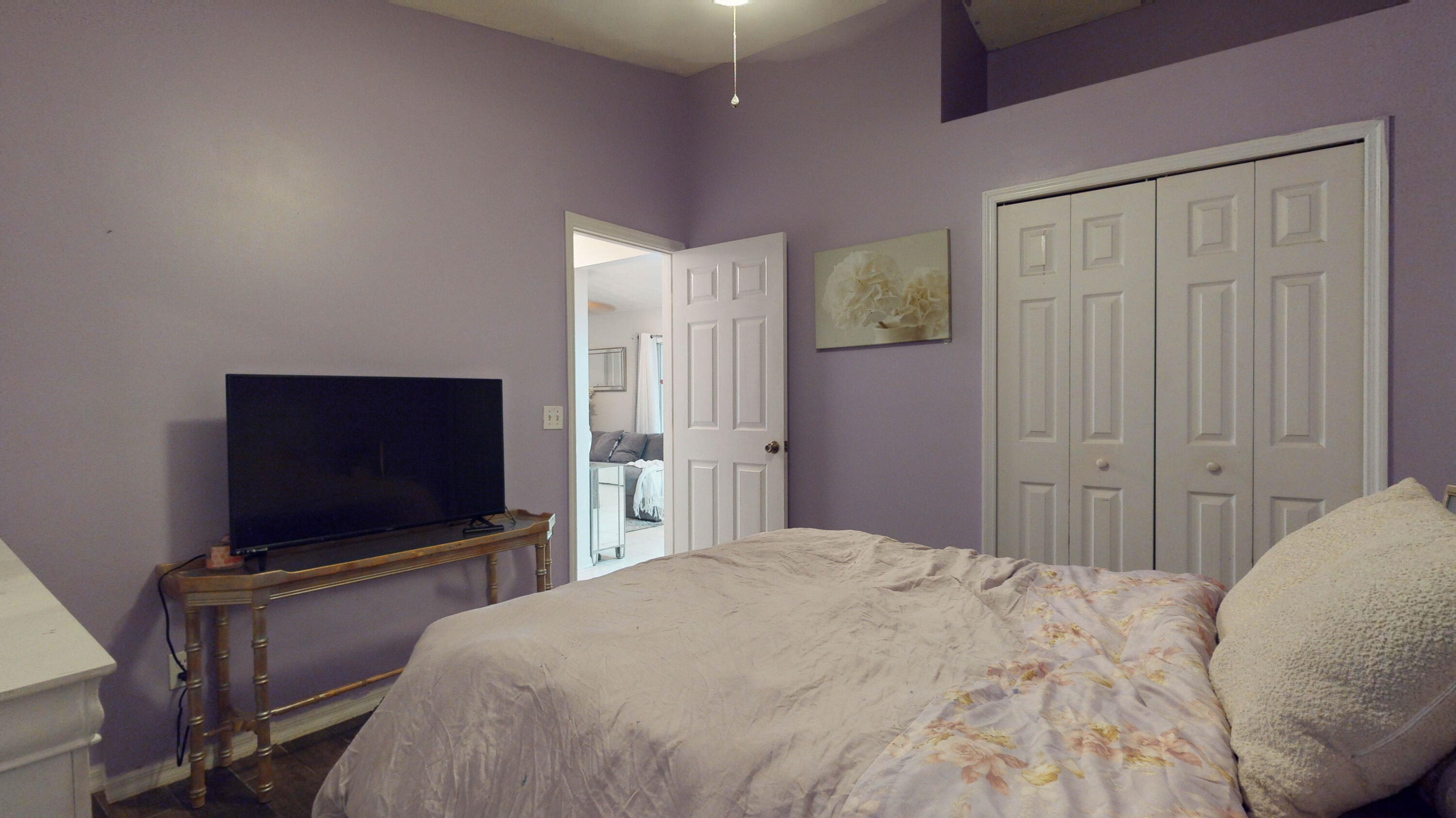 Furnished bedroom with lavender walls, white closet doors, and a television beside the bed.