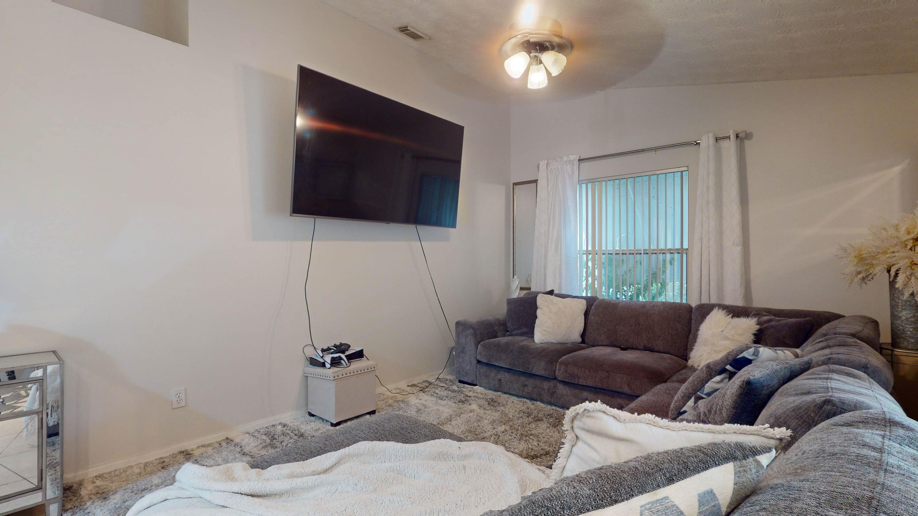 Living room with a gray sectional sofa, wall-mounted television, and sliding glass door.