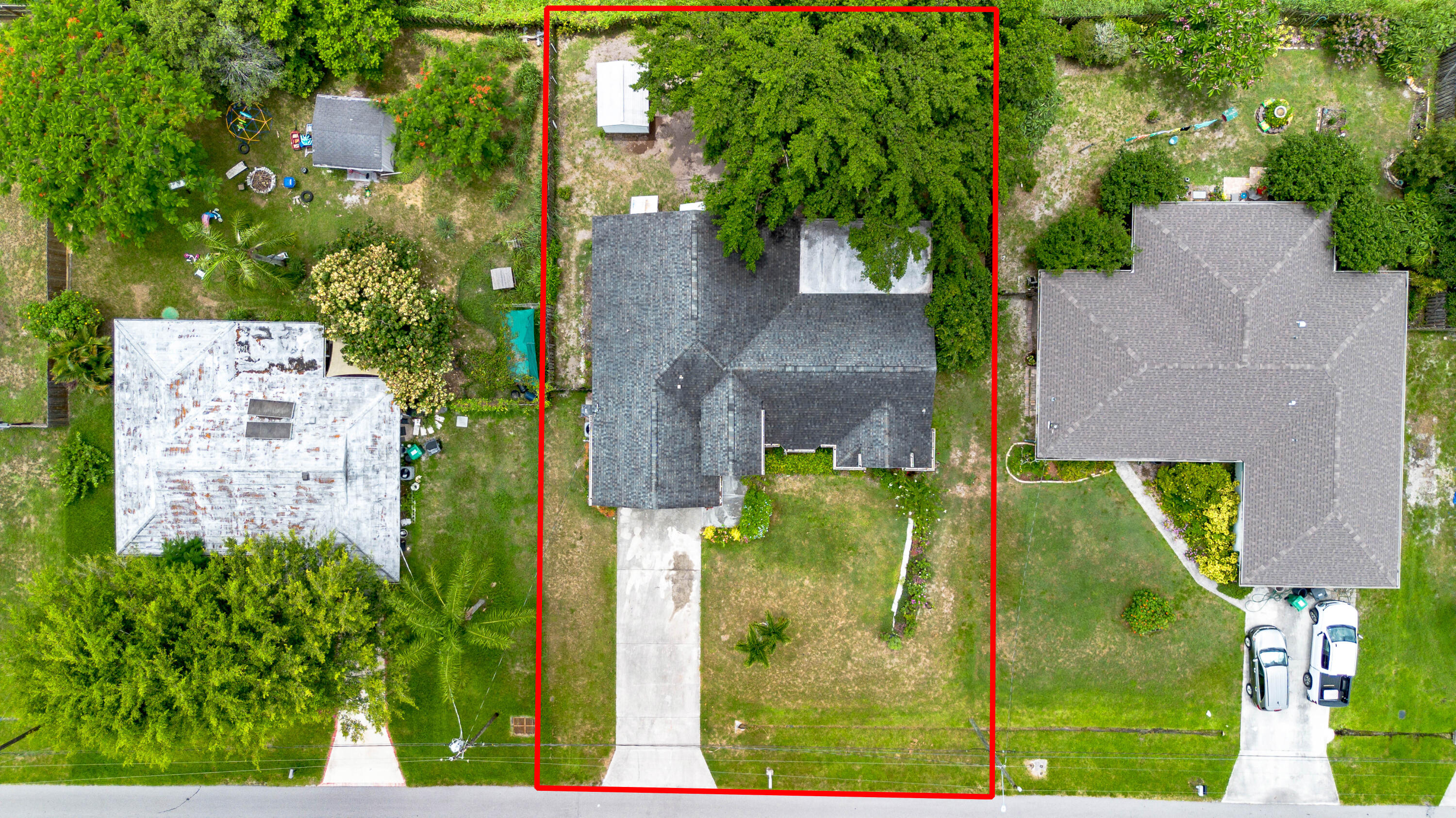 Aerial view of a house and driveway within a red-outlined lot, shaded by a large tree.