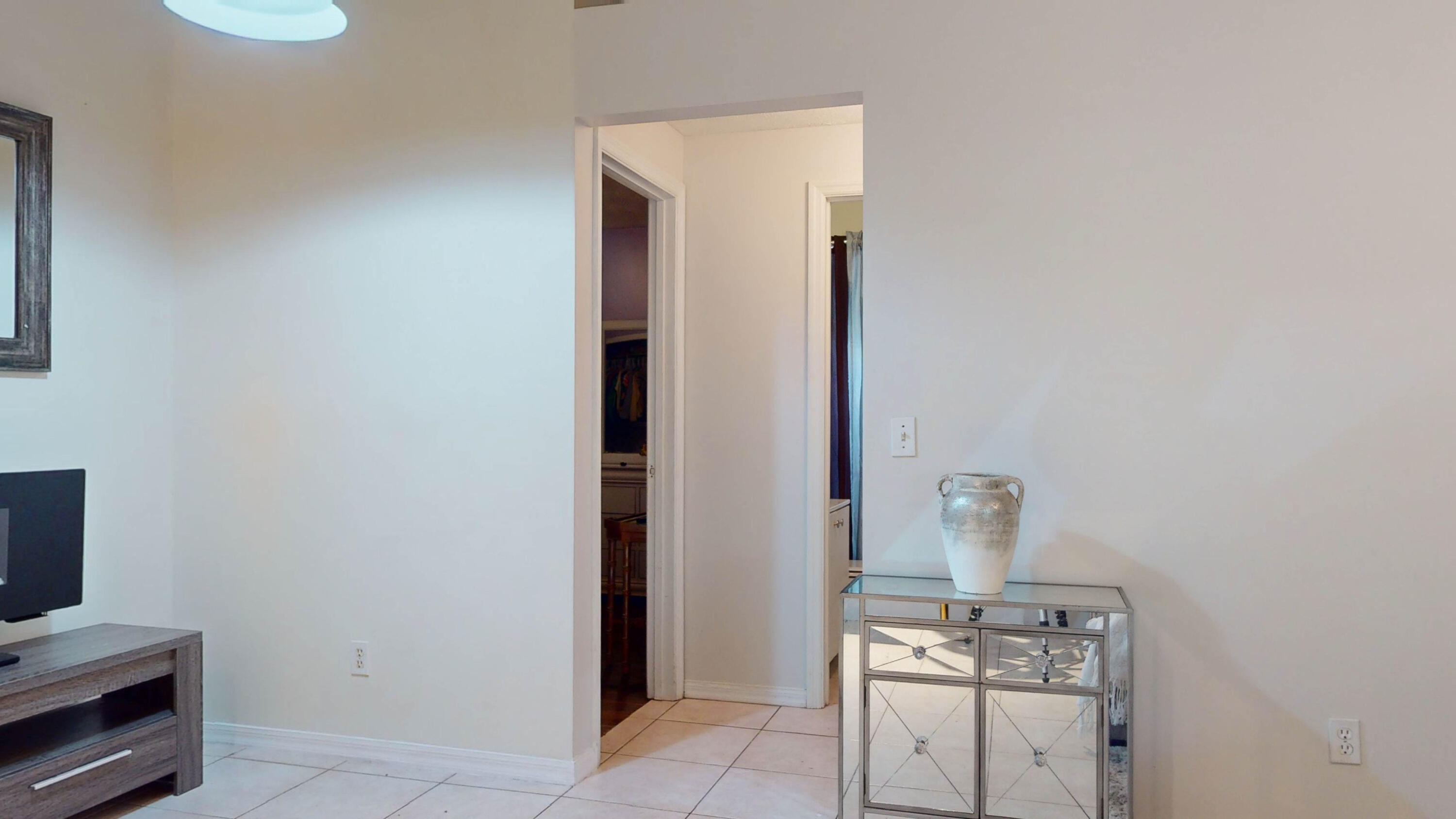 Living room with white tile floors, a television and media console, and a mirrored table beside an open doorway.