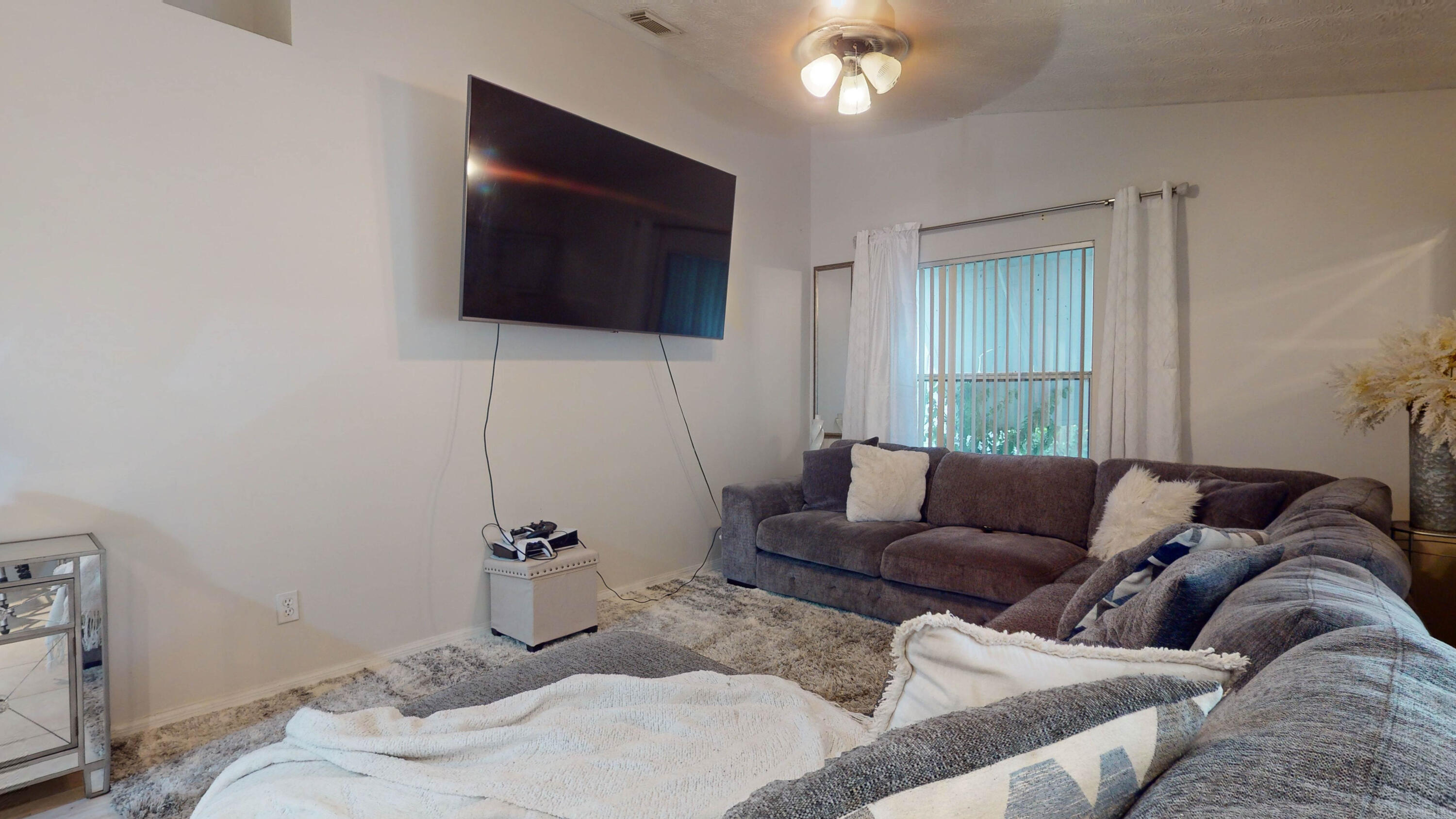 Living room with a gray sectional sofa, wall-mounted television, and curtained window.