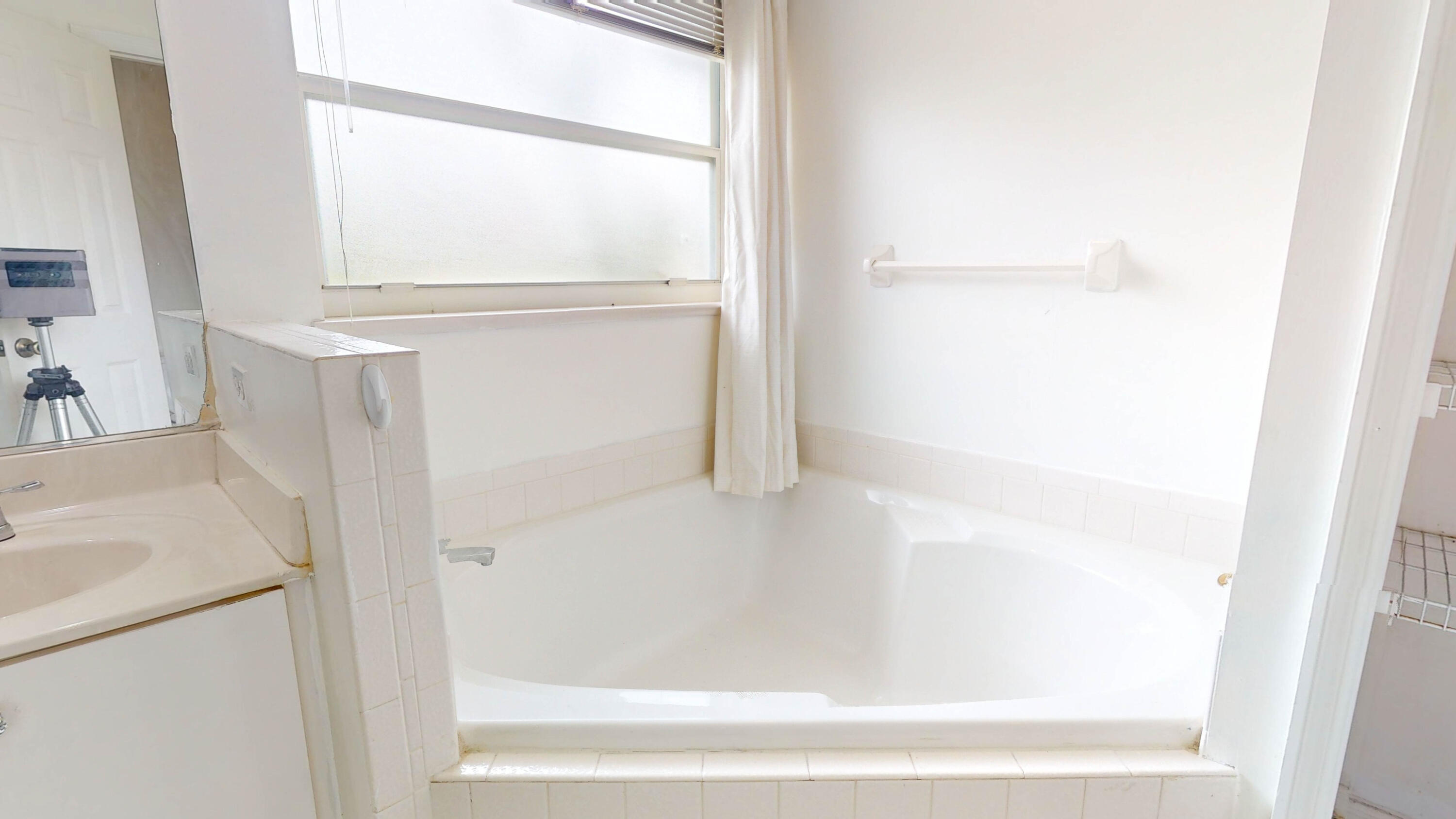 Bathroom with a large white bathtub beneath a window and a grab bar on the wall.
