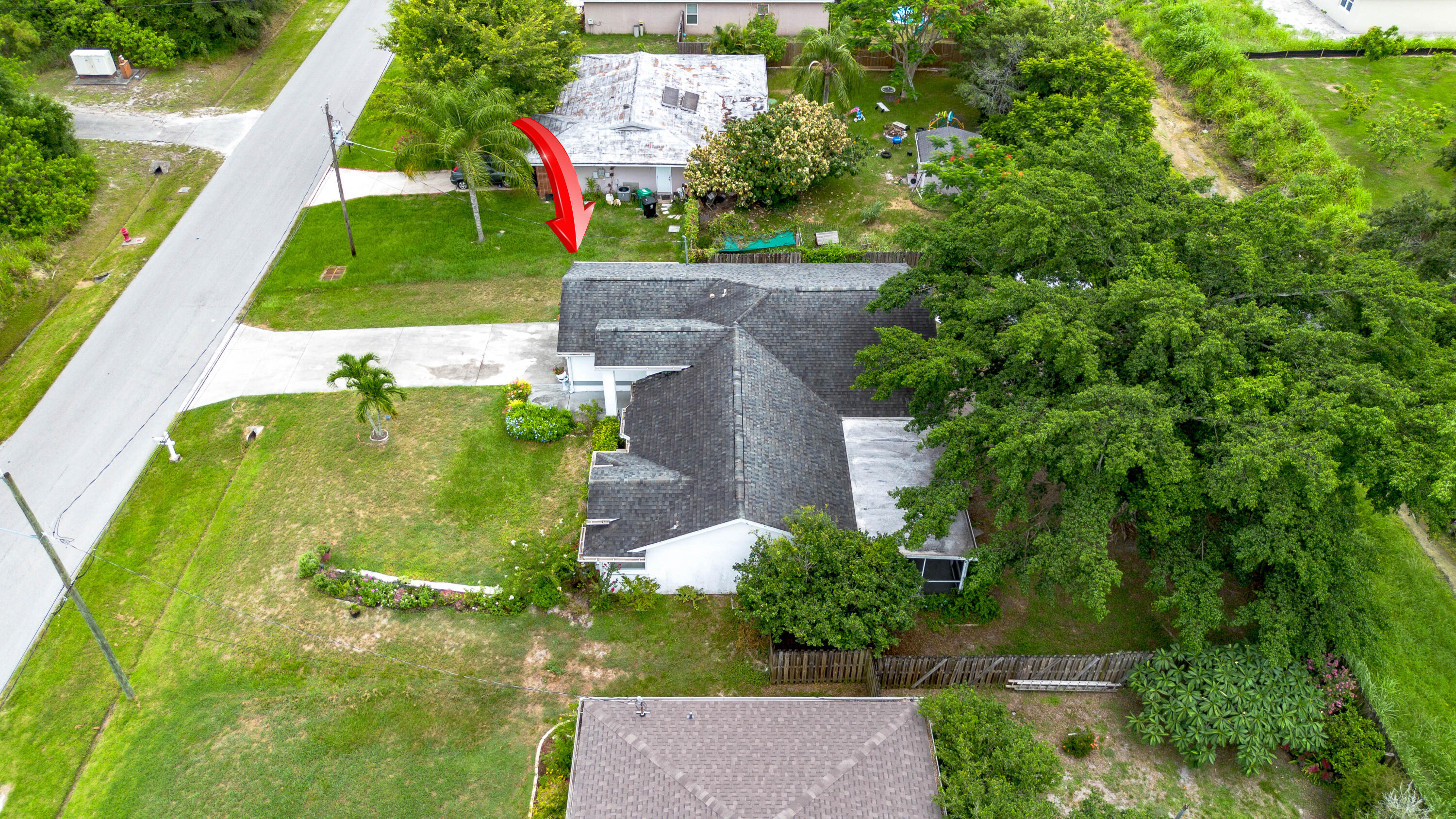 Aerial view of a home and lot, marked by a red arrow, with a broad lawn and mature trees.