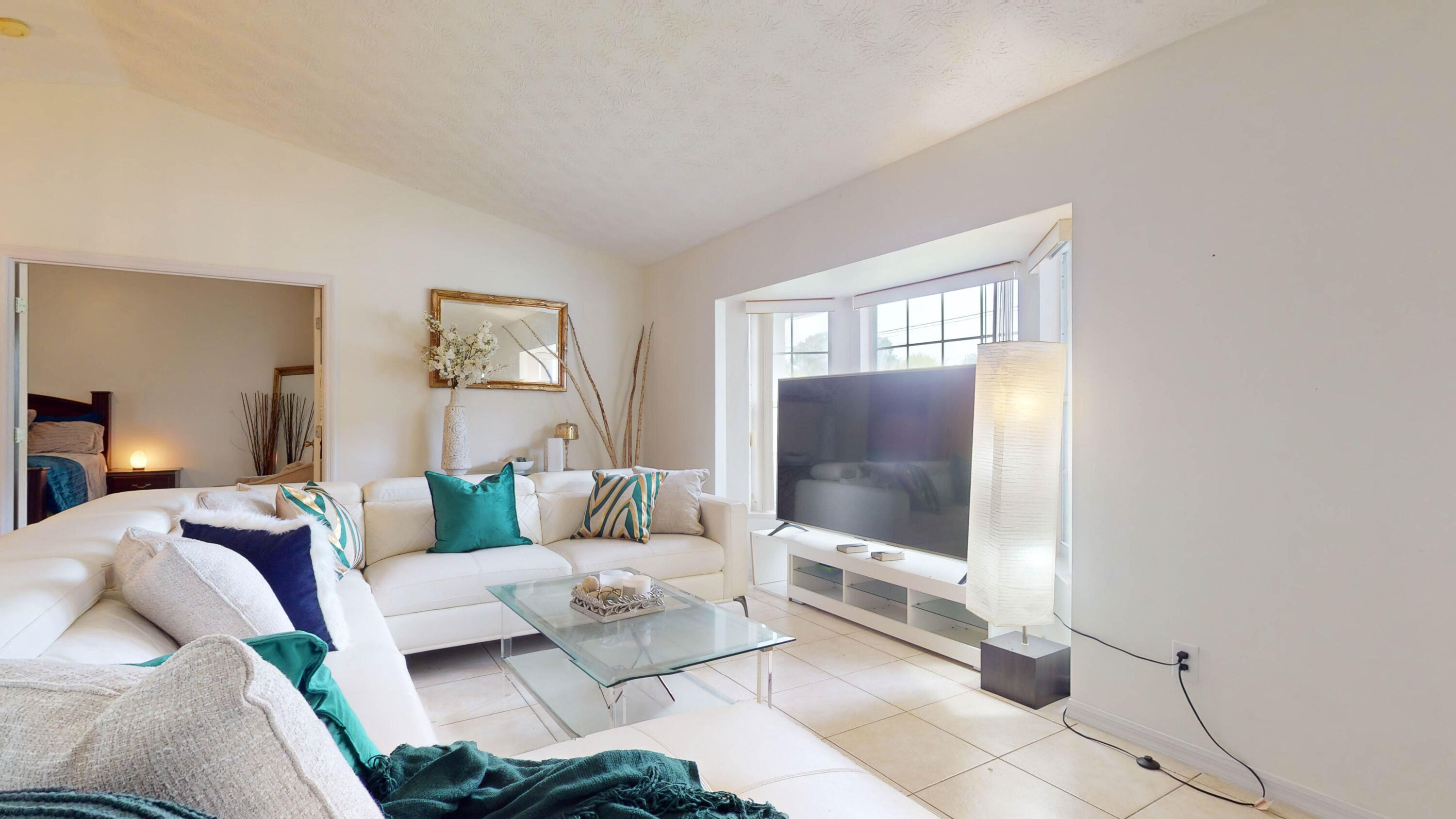 Staged living room with a white sectional sofa, glass coffee table, and large television.