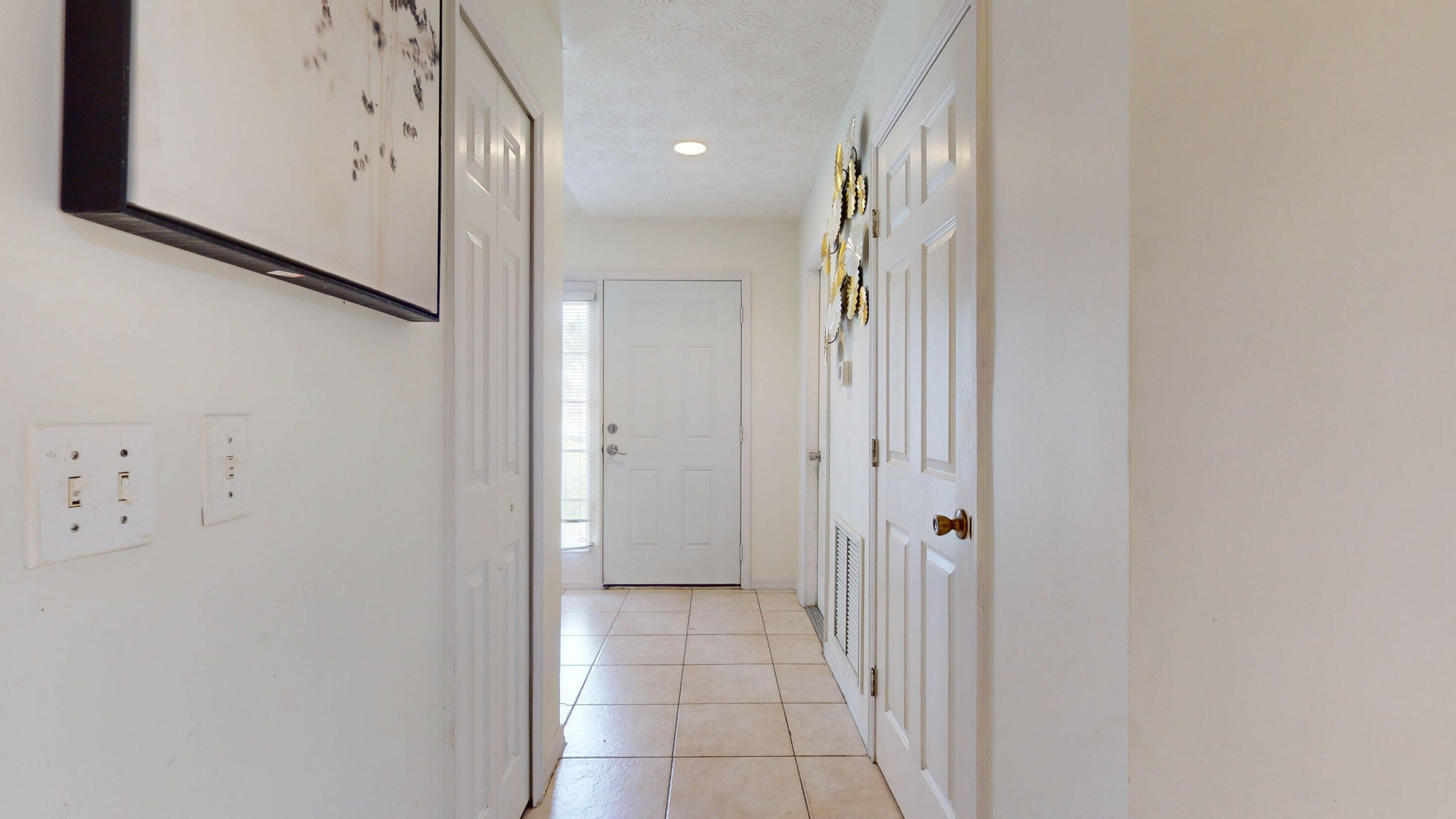 Entry hallway with light tile flooring, white paneled doors, and a front door with a narrow sidelight.
