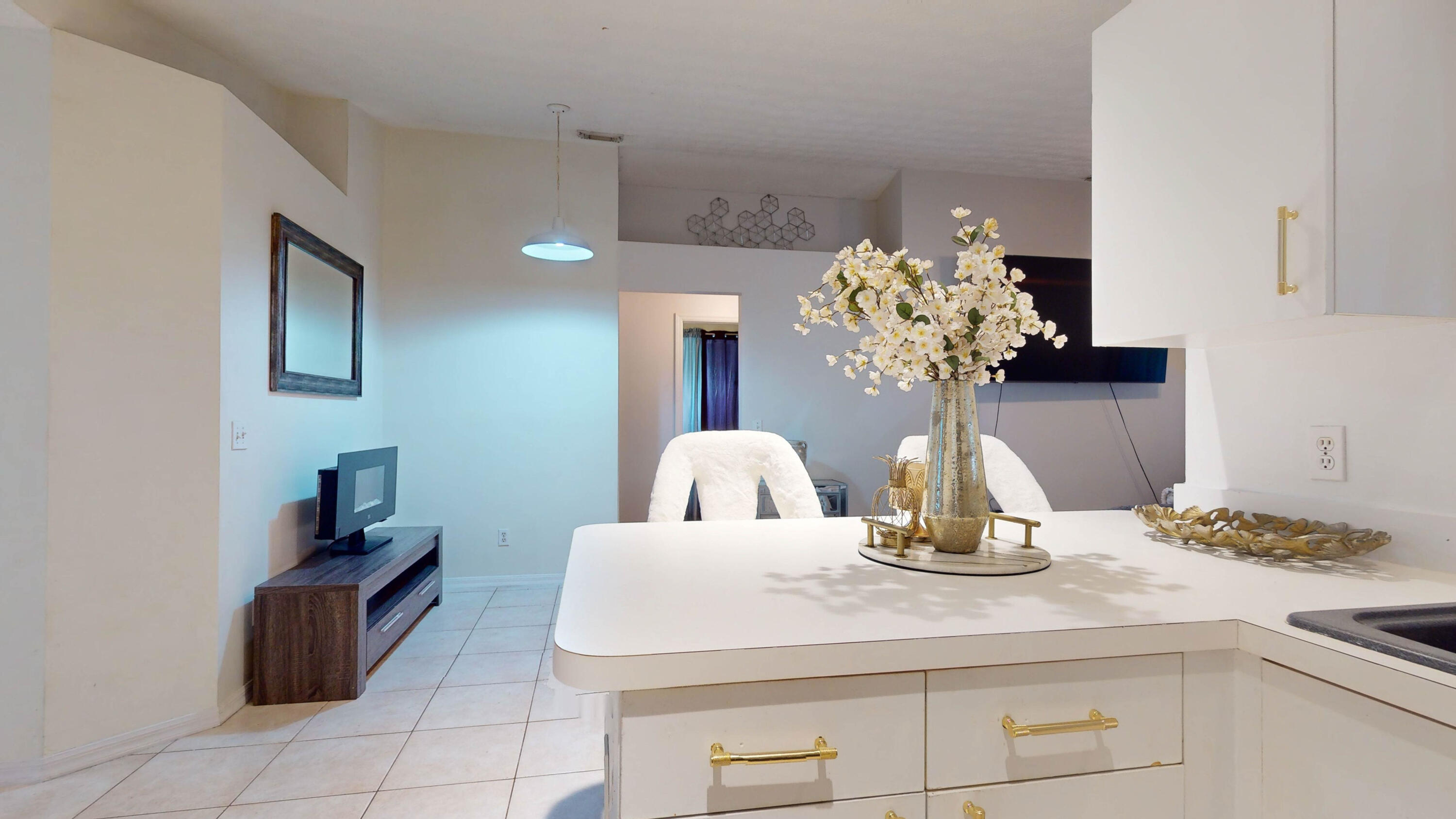 Modern white kitchen peninsula with gold handles and flowers, overlooking an open living area.