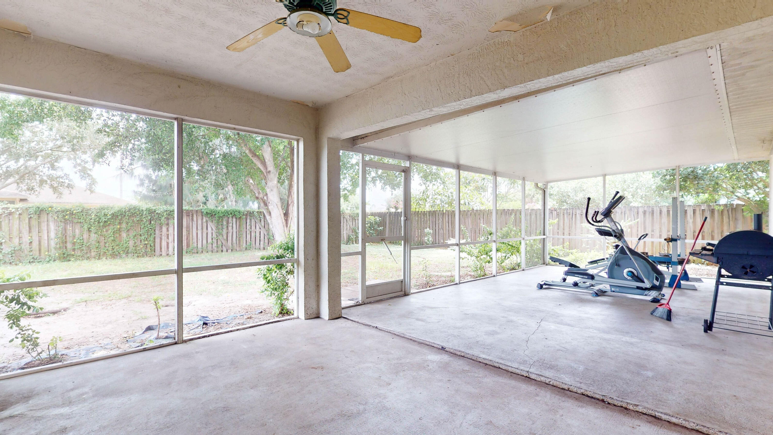 Screened patio with exercise equipment, a ceiling fan, and views of the fenced backyard.