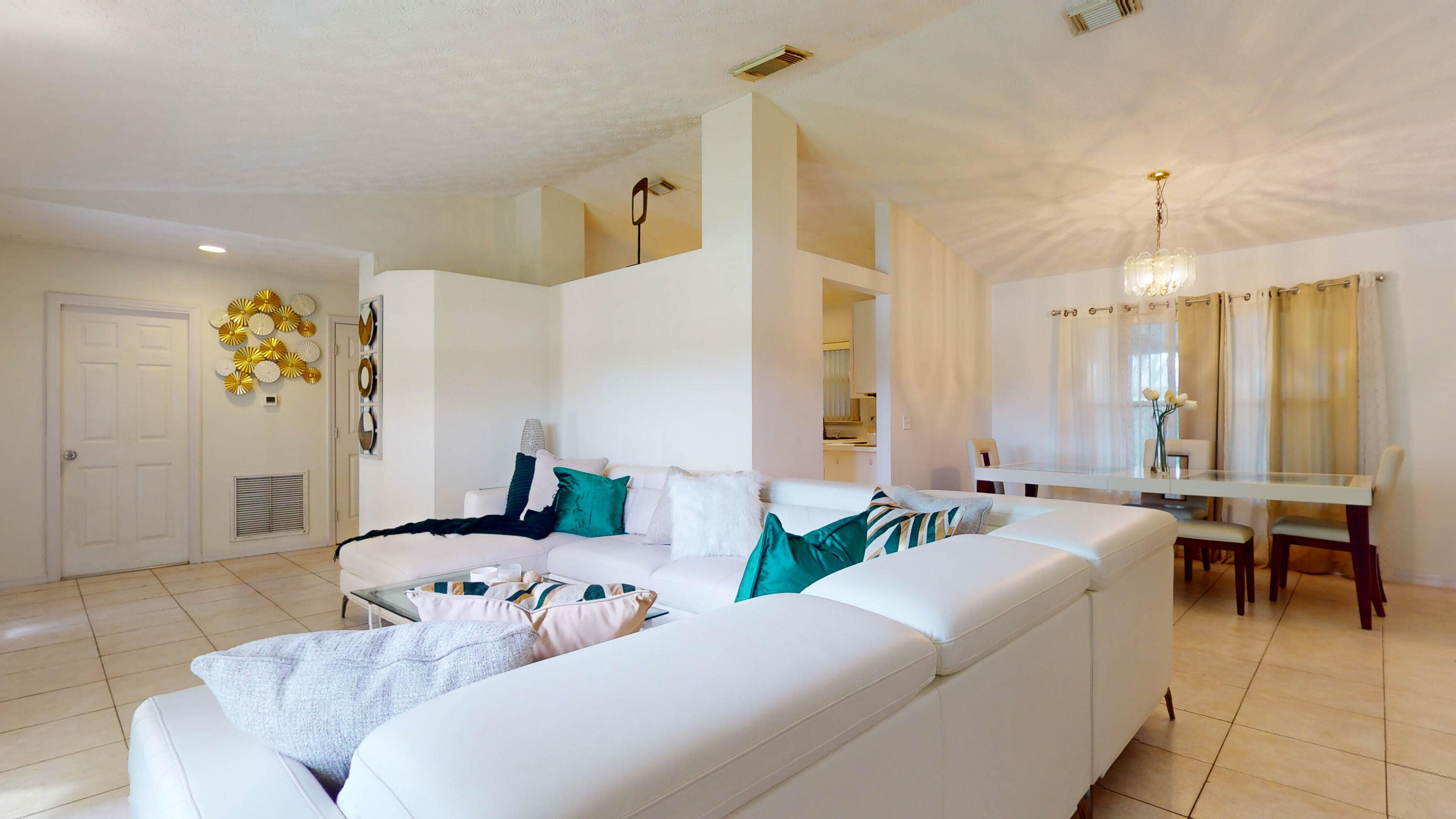 Open-plan living and dining room with a white sectional sofa, tiled floors, and a chandelier.