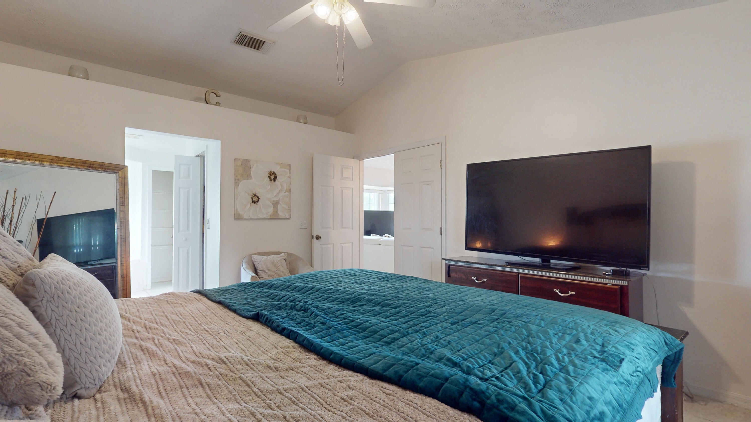 Furnished bedroom with a teal-covered bed and large television on a dresser.