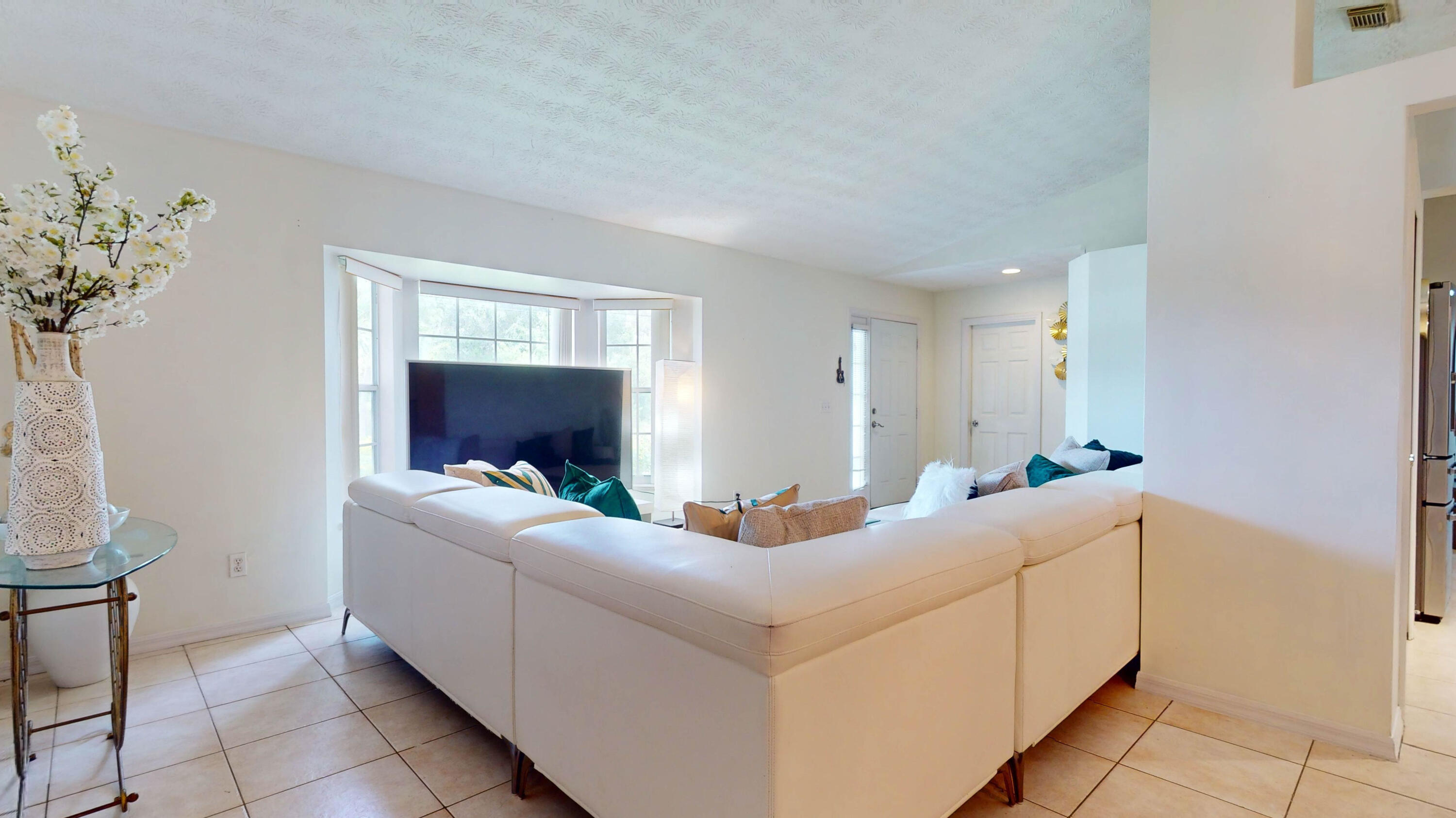 Furnished living room with a white sectional, television, and bright bay windows.