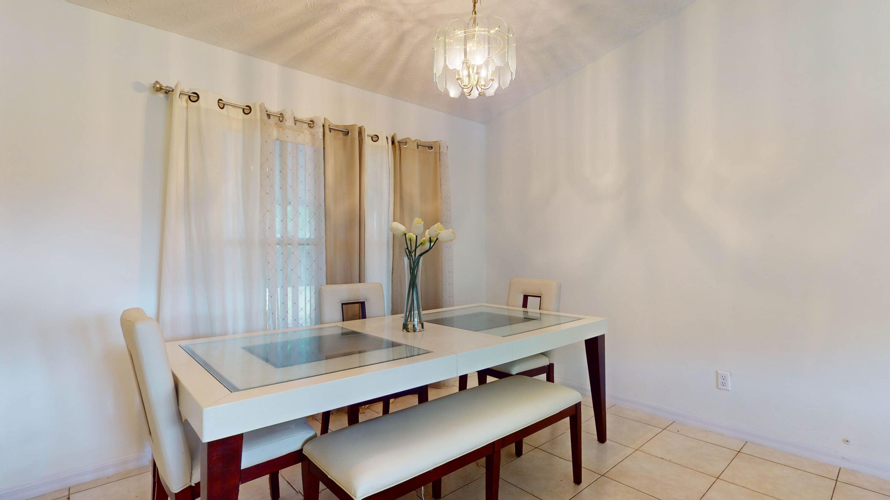 Dining room with a glass-top table, cream seating, beige curtains, and a chandelier.