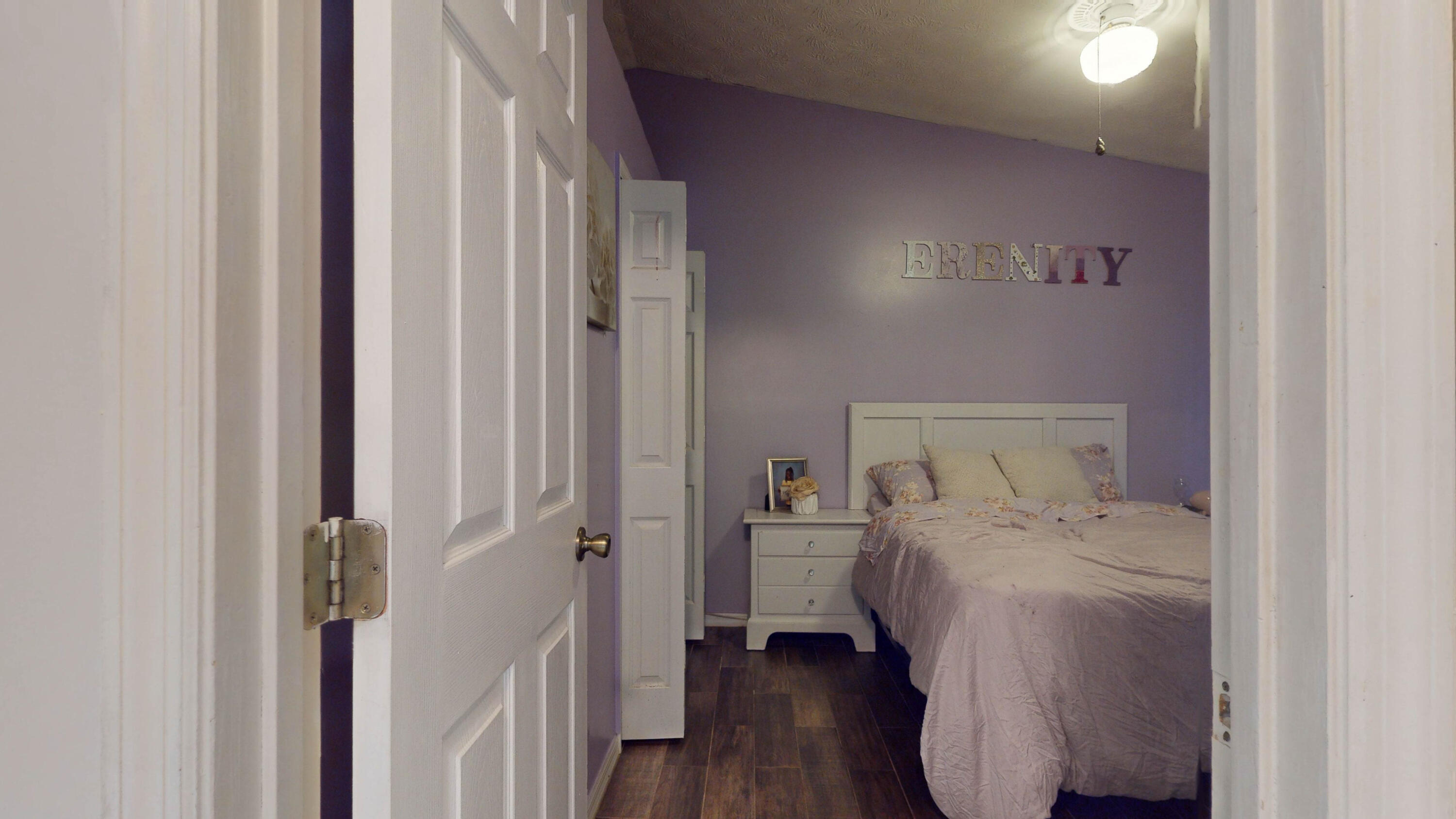 Bedroom with lavender walls, floral bedding, and “SERENITY” lettering above the bed.