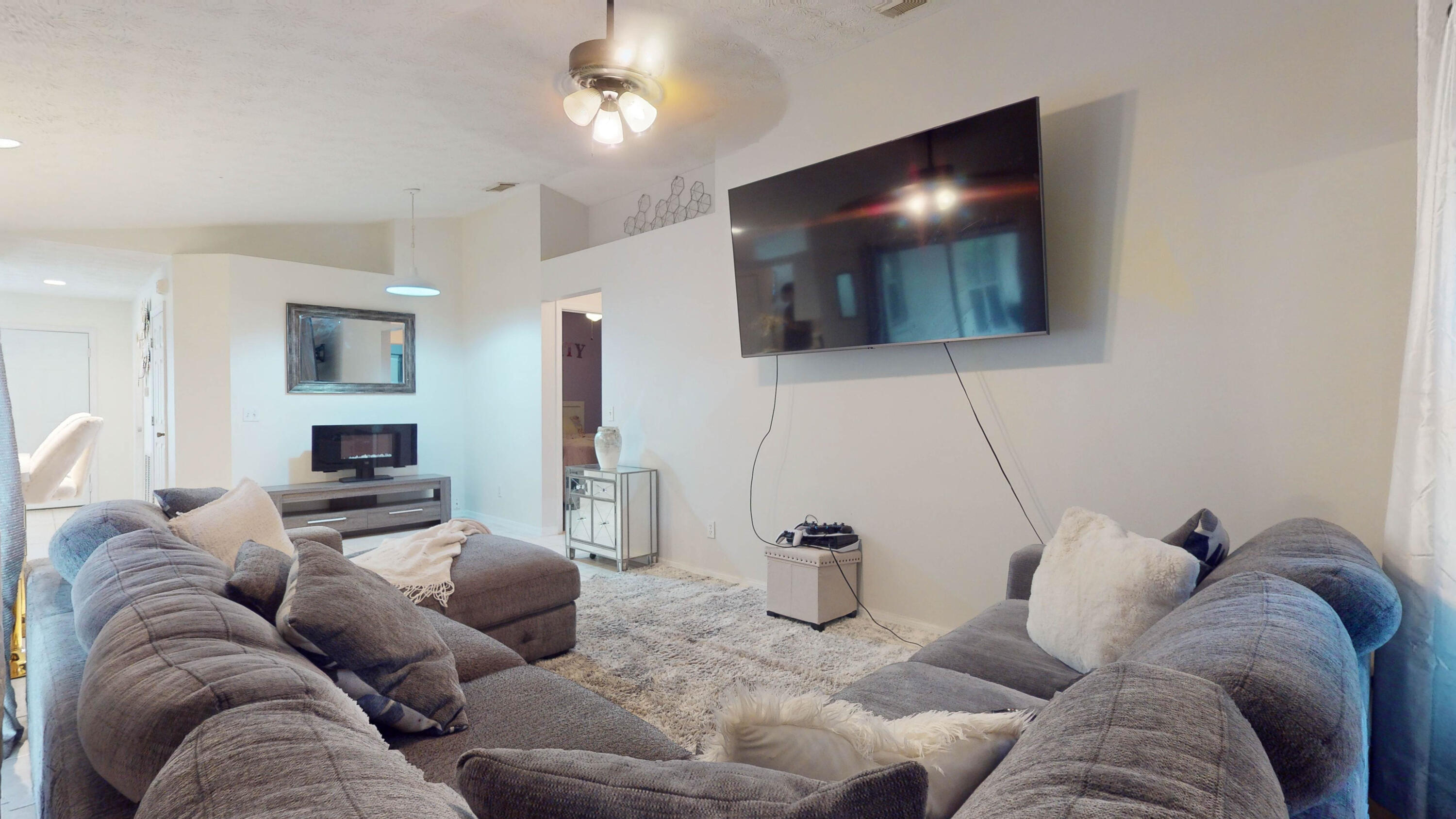 Living room with gray sectional sofas, a large wall-mounted TV, and a pale shag rug.