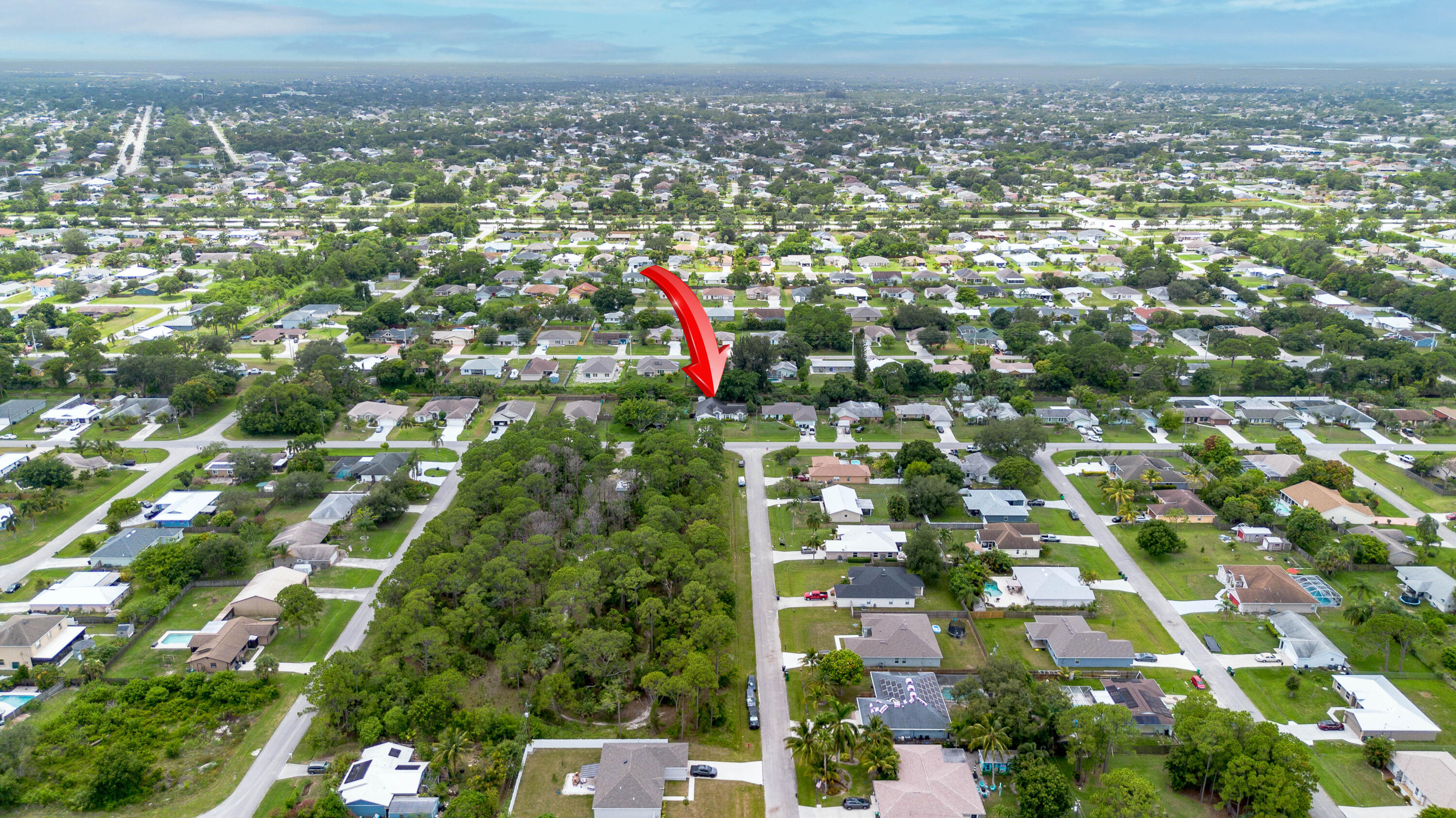 Aerial view of a suburban neighborhood, with a red arrow marking a home beside wooded land.