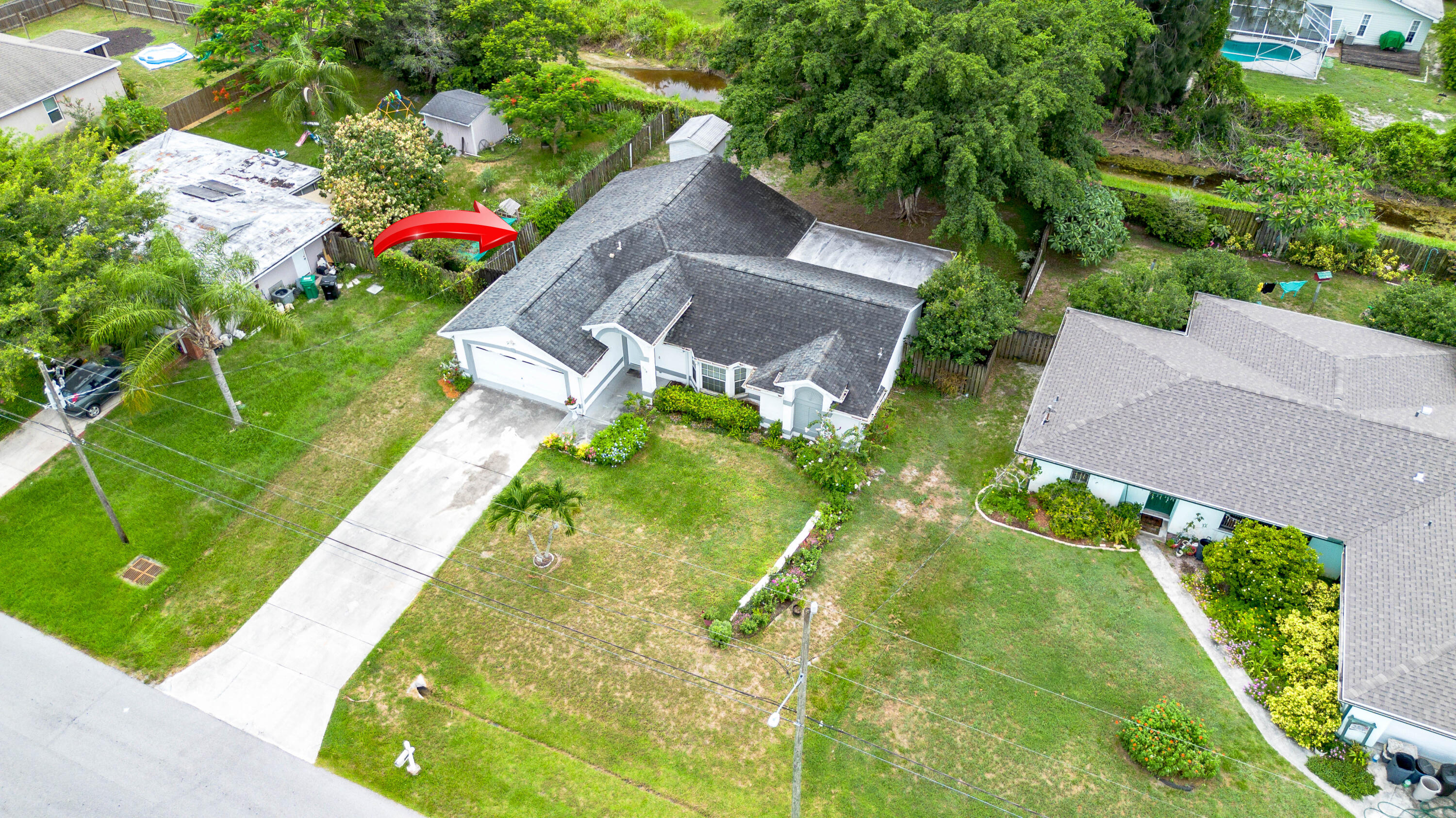 Aerial view of a white single-story home with a gray roof and driveway, marked by a red arrow.
