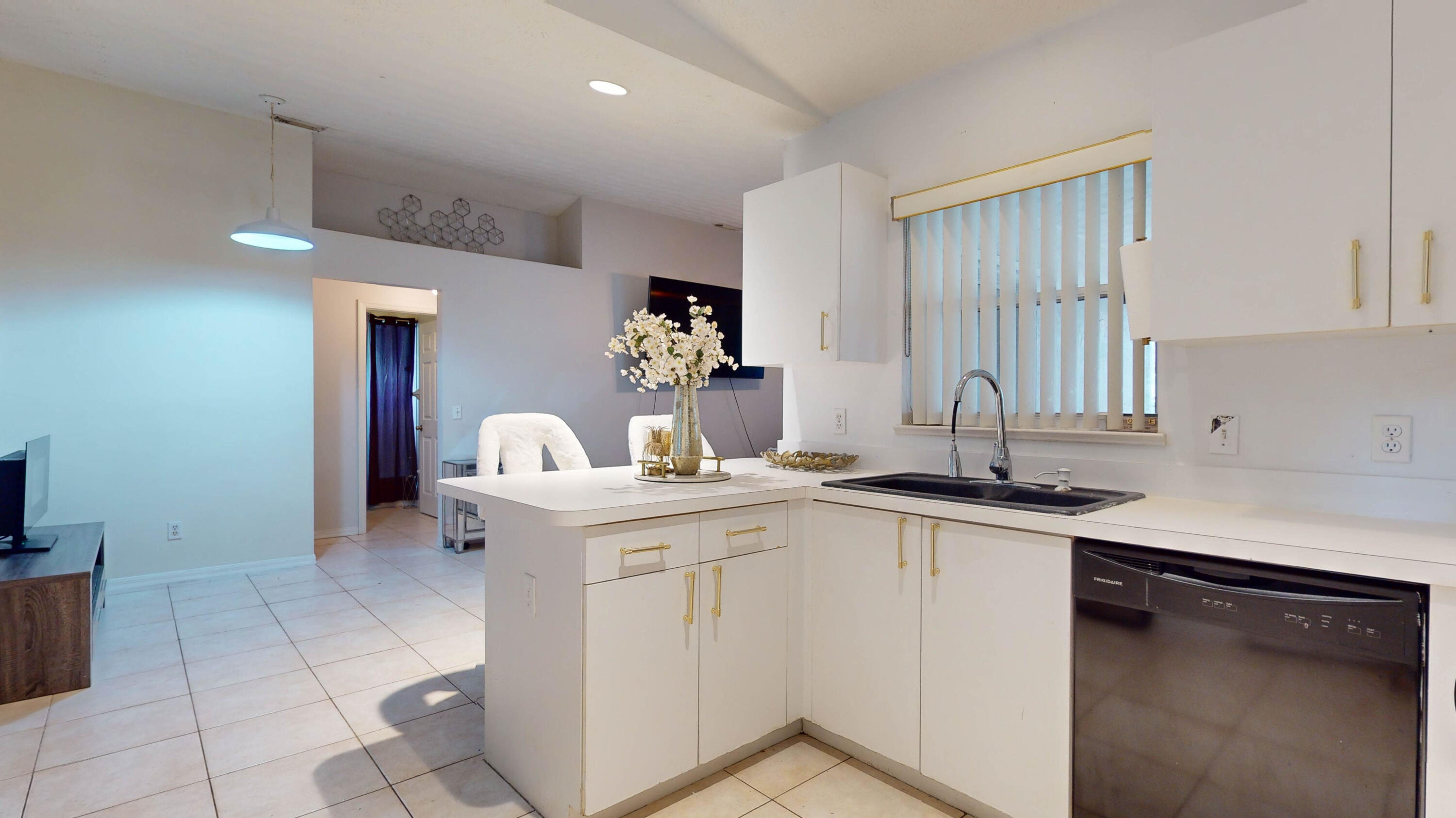 Bright white kitchen with gold-tone cabinet pulls, breakfast bar, double sink, and dishwasher.